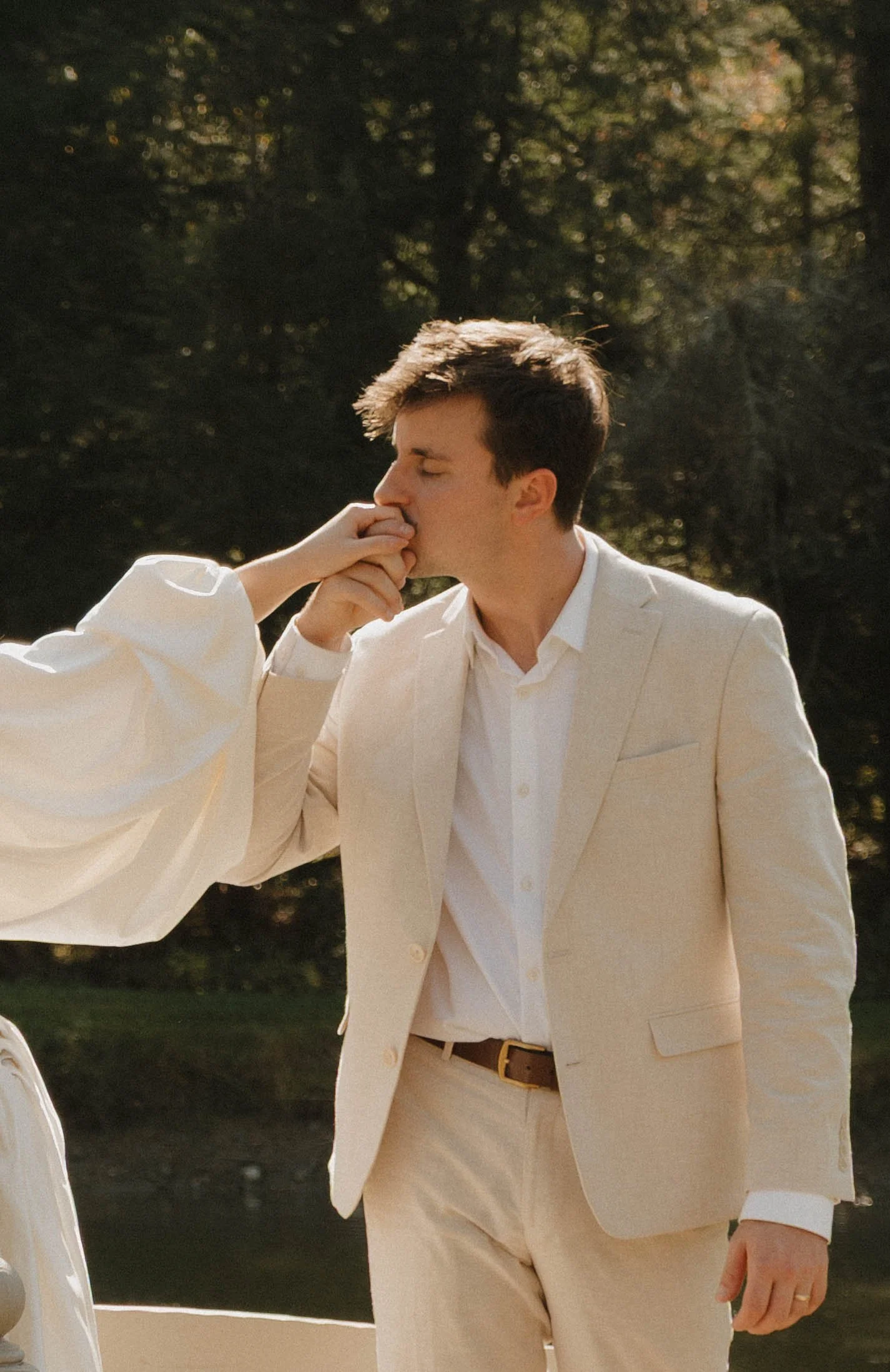 A groom kissing the back of his bride's hand outdoors during daytime.