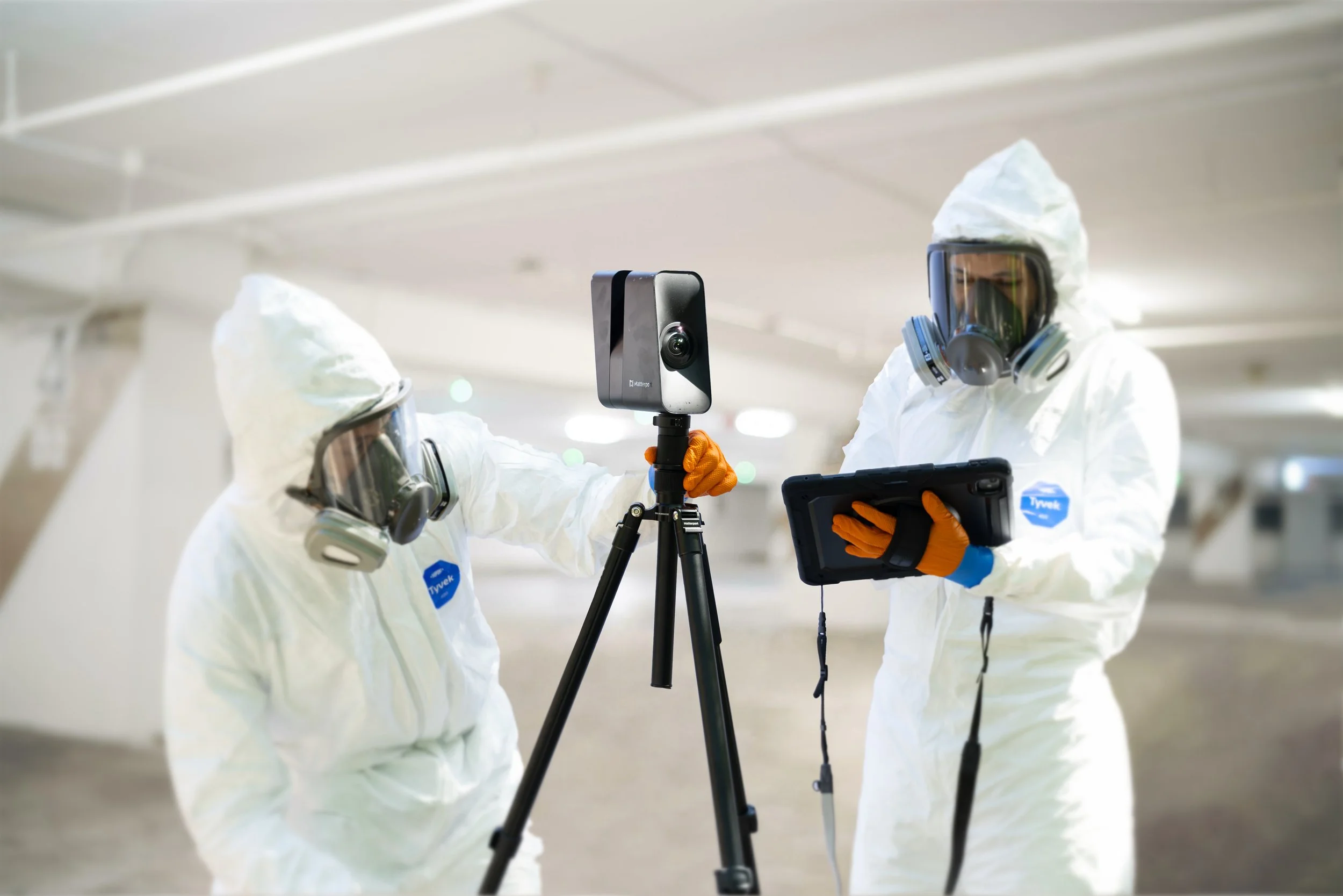 Licensed mold assessors in coveralls and full-face respirators setting up a Matterport 3D camera on a tripod during a mold assessment.