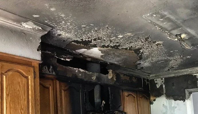 Burn damage on kitchen ceiling and wall above wooden cabinets.