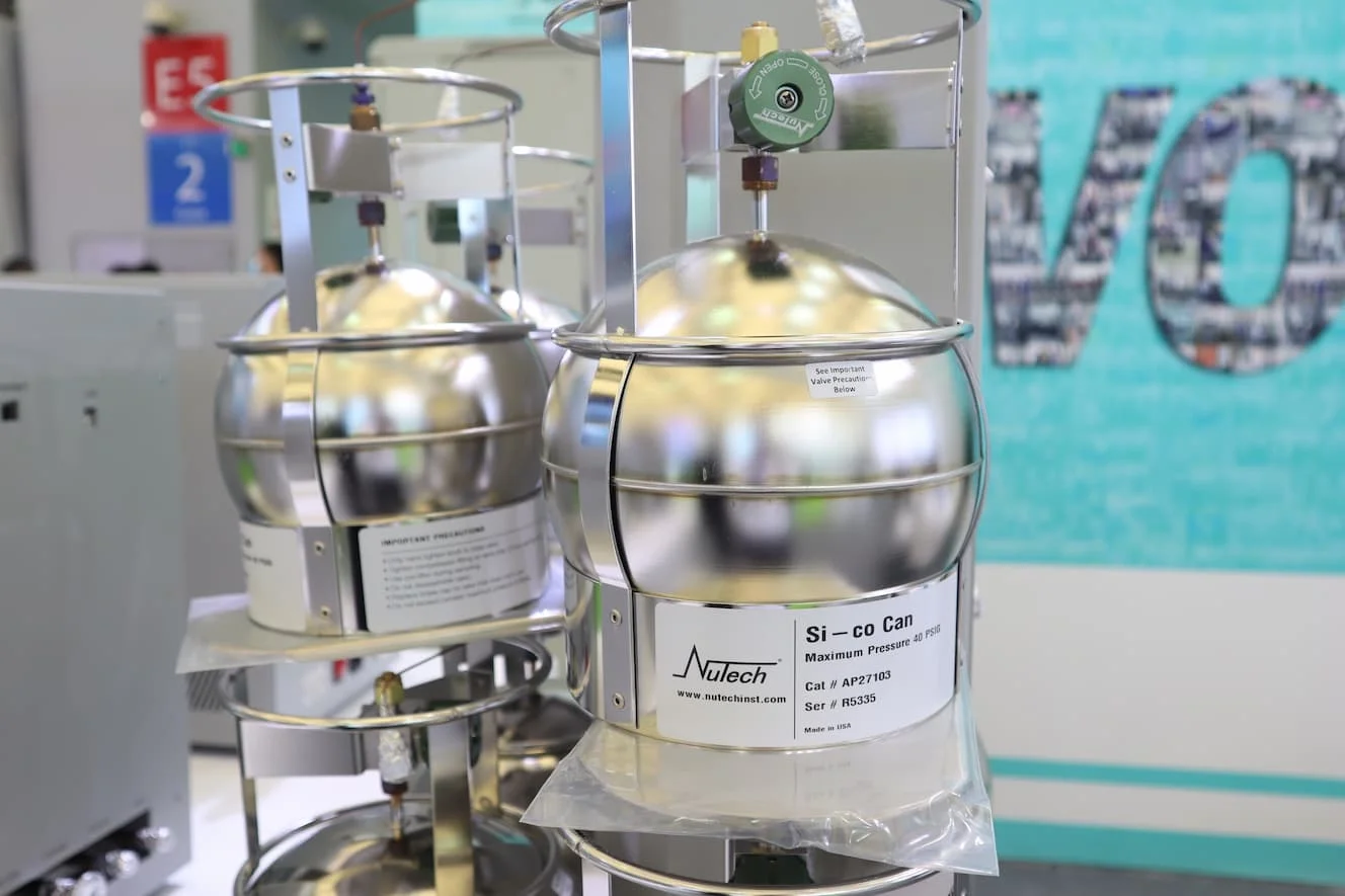 A nitrogen co2 canister used for scientific purposes, with a metallic spherical body and associated pressure gauge, labeled Nulech, displayed in an indoor laboratory or industrial setting.