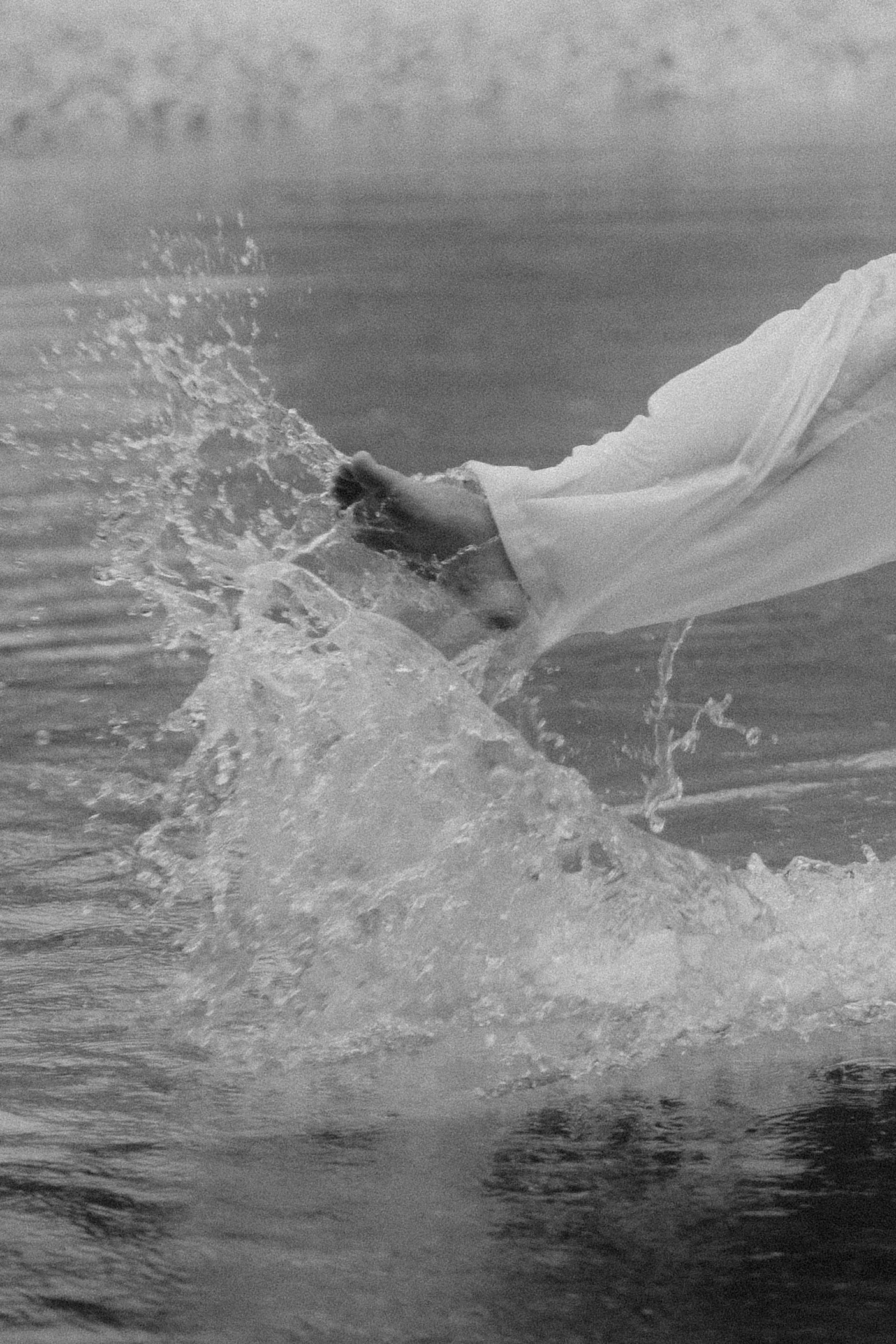 Eine Hand in einem weißen Kleid oder Hemd taucht ins Wasser, erzeugt Wasser spritzende Bewegungen.