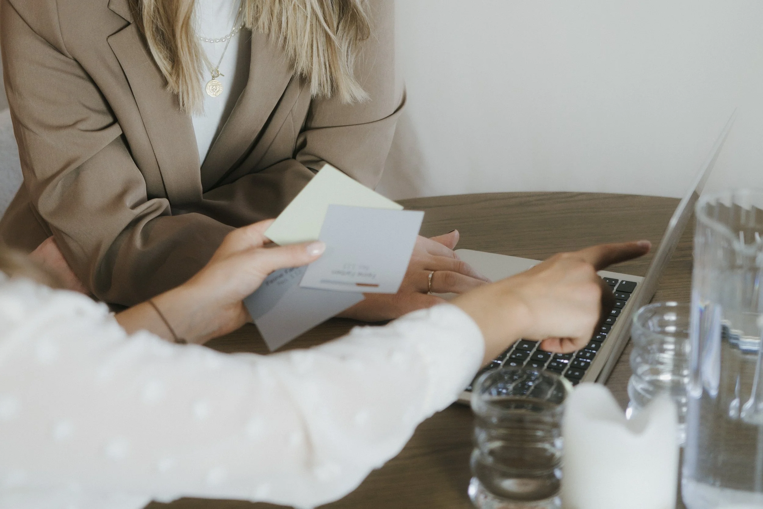 Zwei Frauen arbeiten gemeinsam an einem Laptop bei einem Business-Treffen. Eine Frau zeigt auf den Laptop, während die andere eine Broschüre hält.