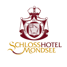 Das Logo des Schloss Hotel Mondsee, das einen Wappen mit Krone und das Hotel im Schild zeigt, mit goldener und brauner Schrift.