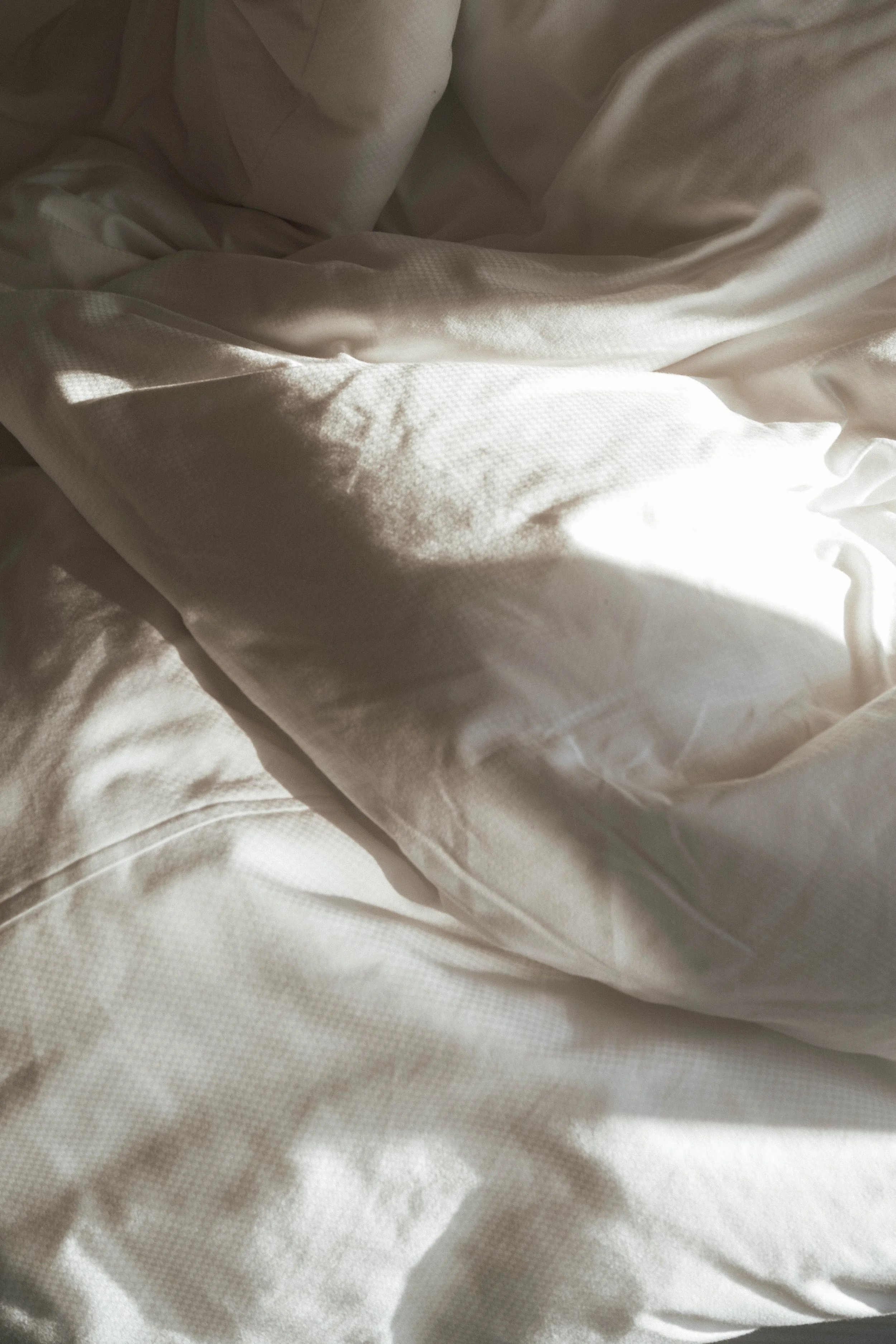 Weiche, weiße Bettwäsche mit Sonnenschein, der auf die Oberfläche fällt.