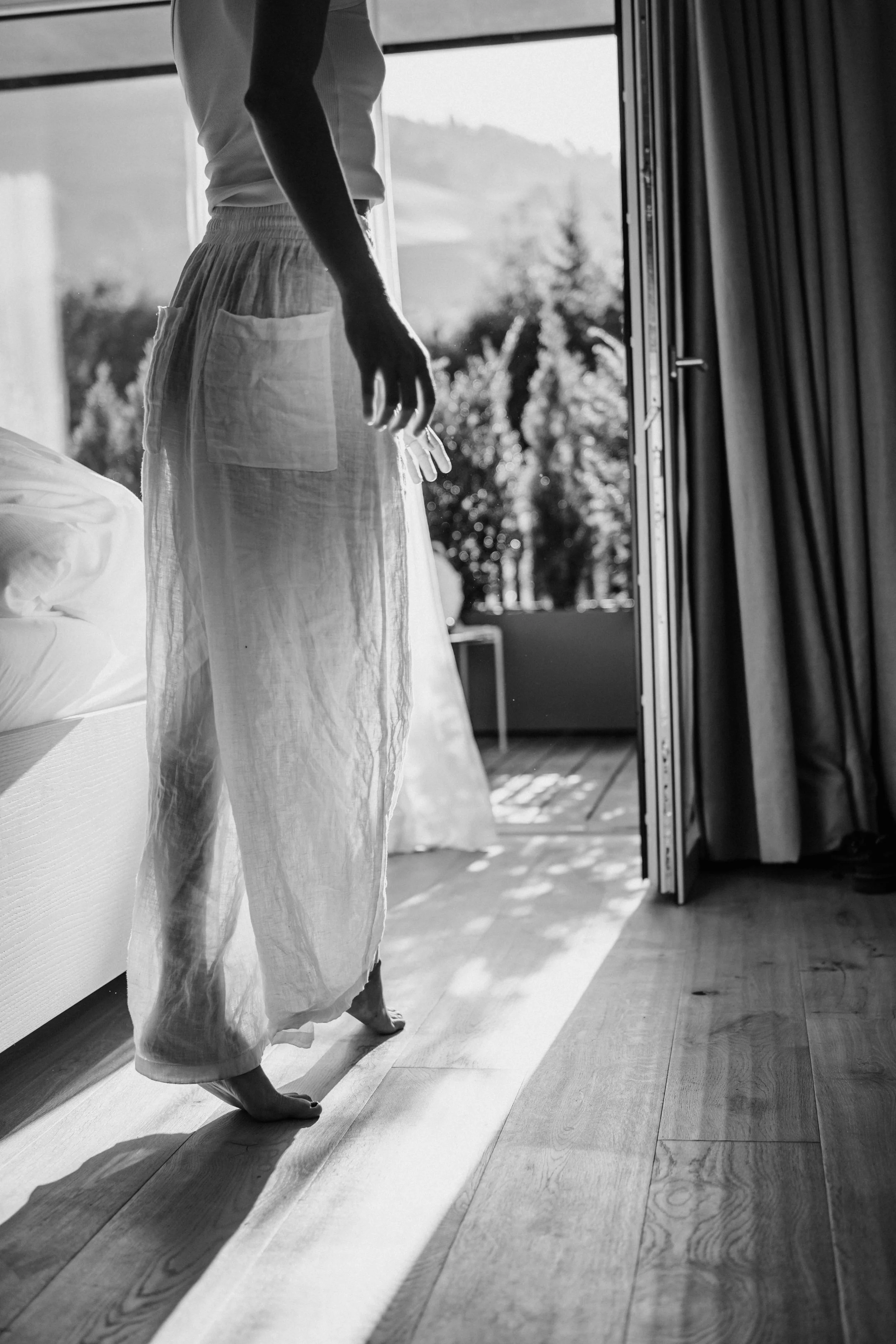 Eine Person steht barfuß auf Holzboden in einem Raum, das Licht scheint durch eine große Tür nach draußen.