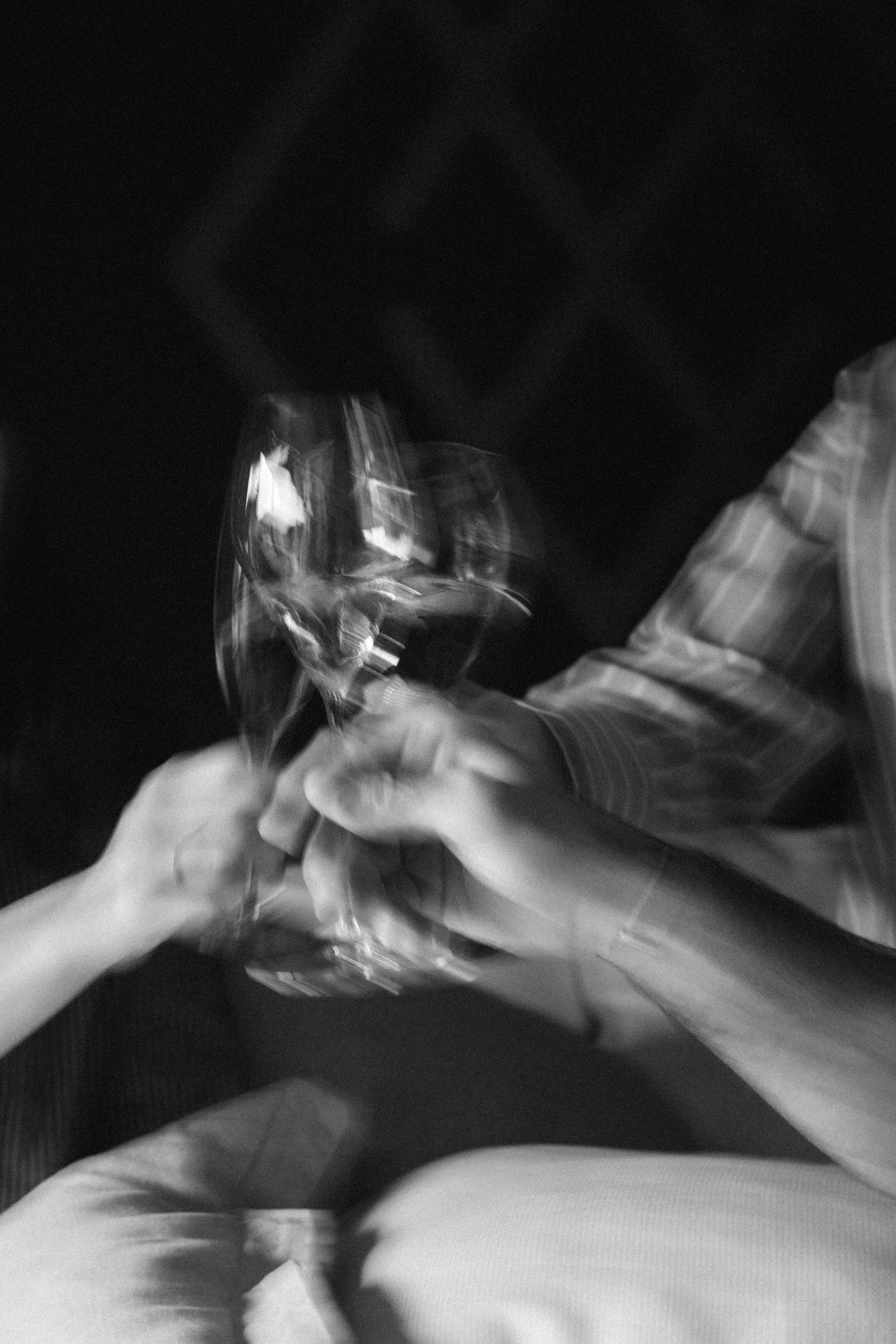 Zwei Personen halten Gläser mit Wein und stoßen an, auf einem schwarzen Hintergrund, in schwarz-weiß aufgenommen.