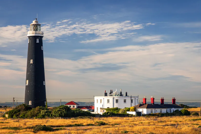 The lighthouse at Dungeness set against blue skies with the sea in the backround.