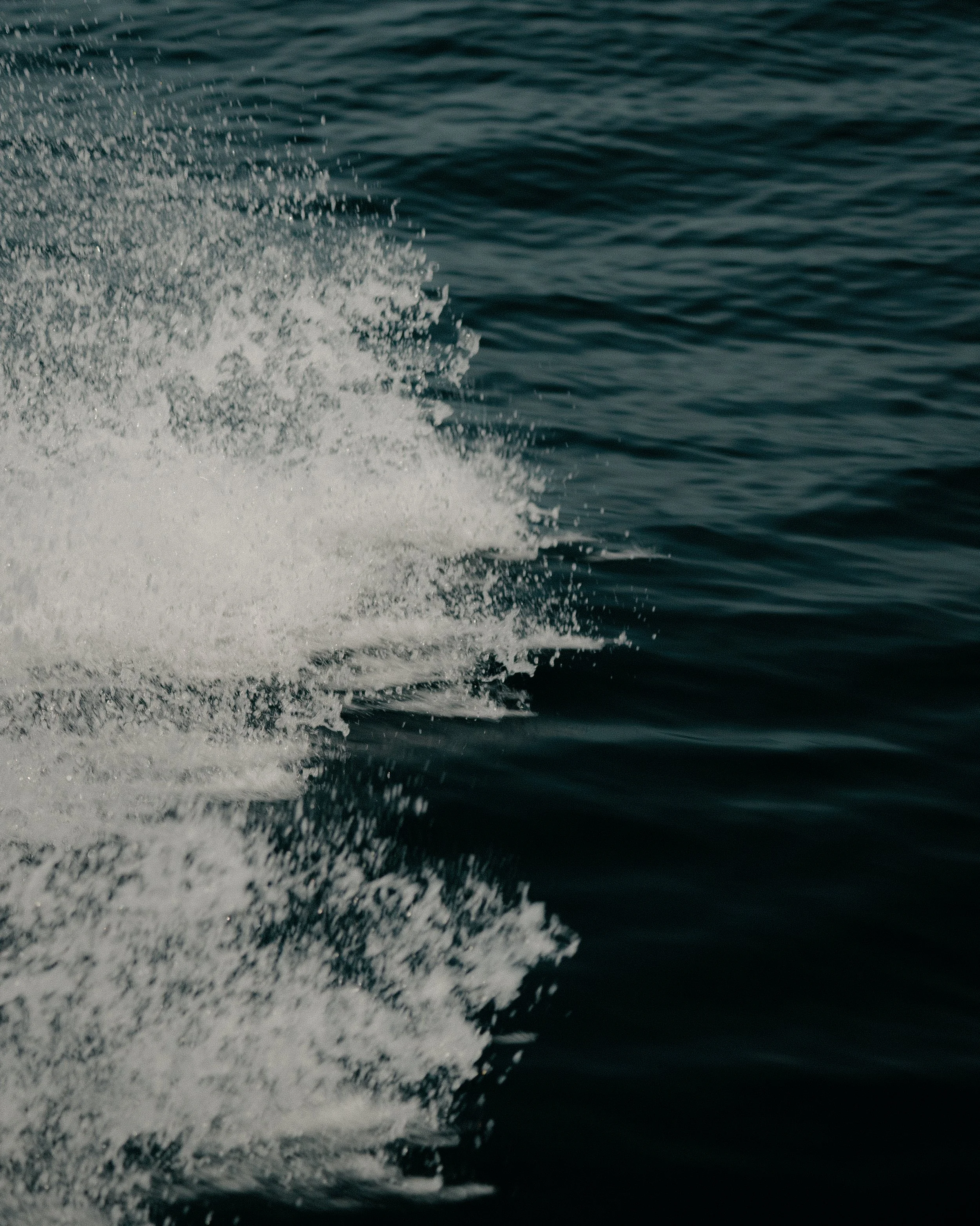 Photo of water with a boat's wake creating splashes and ripples on the surface.