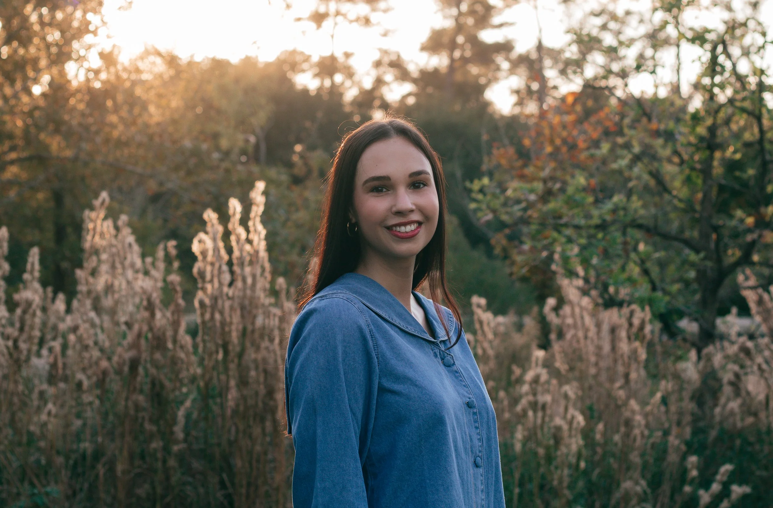 Natural light portrait in a fall landscape, featuring person in blue shirt surrounded by warm tones and soft sunset glow.