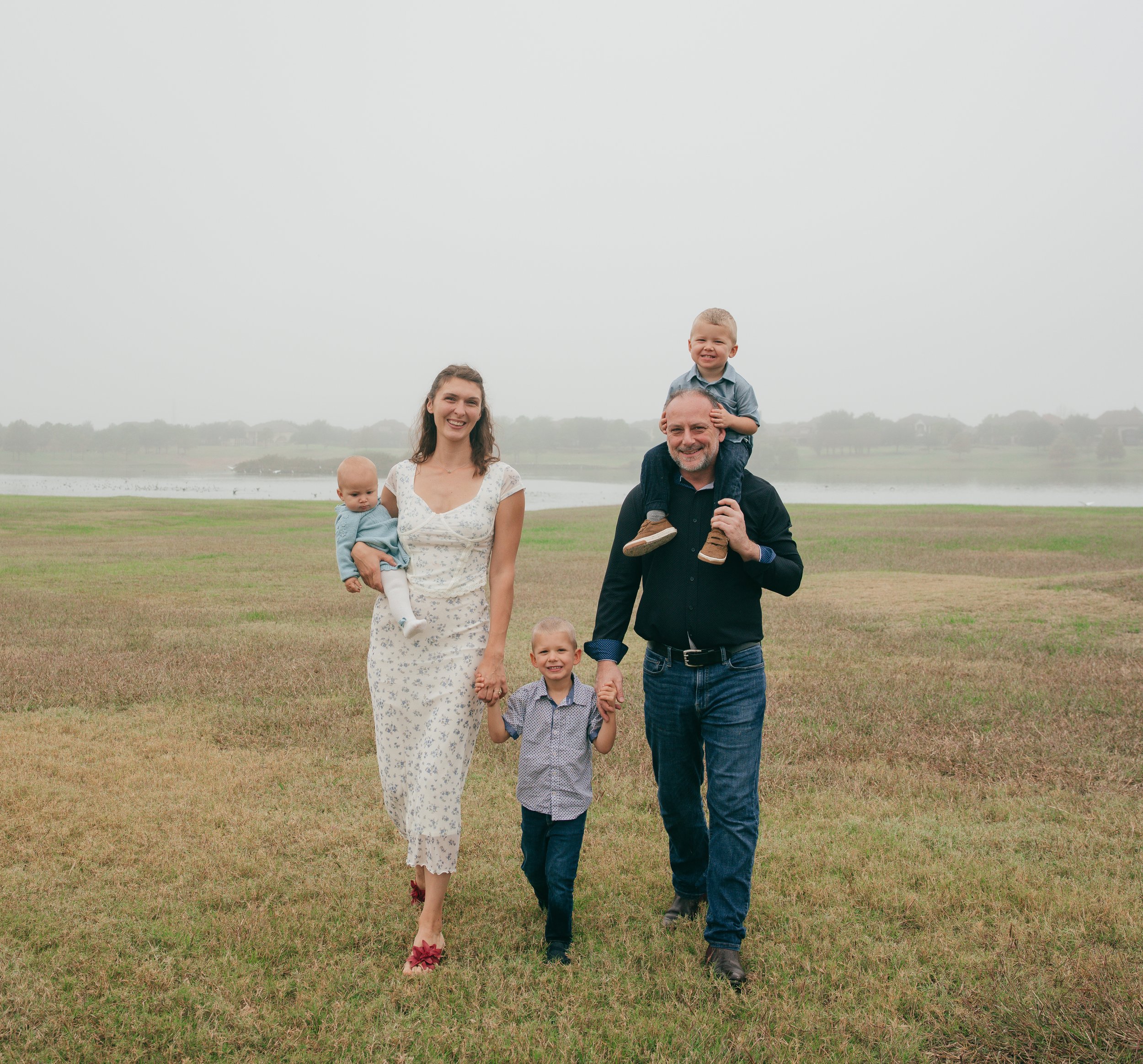 Stylish family portrait in motion, walking through an overcast landscape with a fog‑covered lake fading behind them.