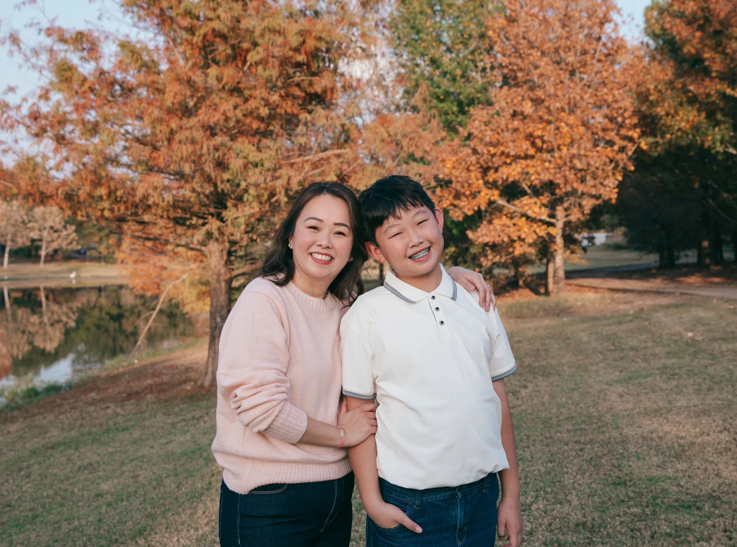 Warm family photo of mother and son smiling together, surrounded by bright autumn leaves in a scenic outdoor setting.