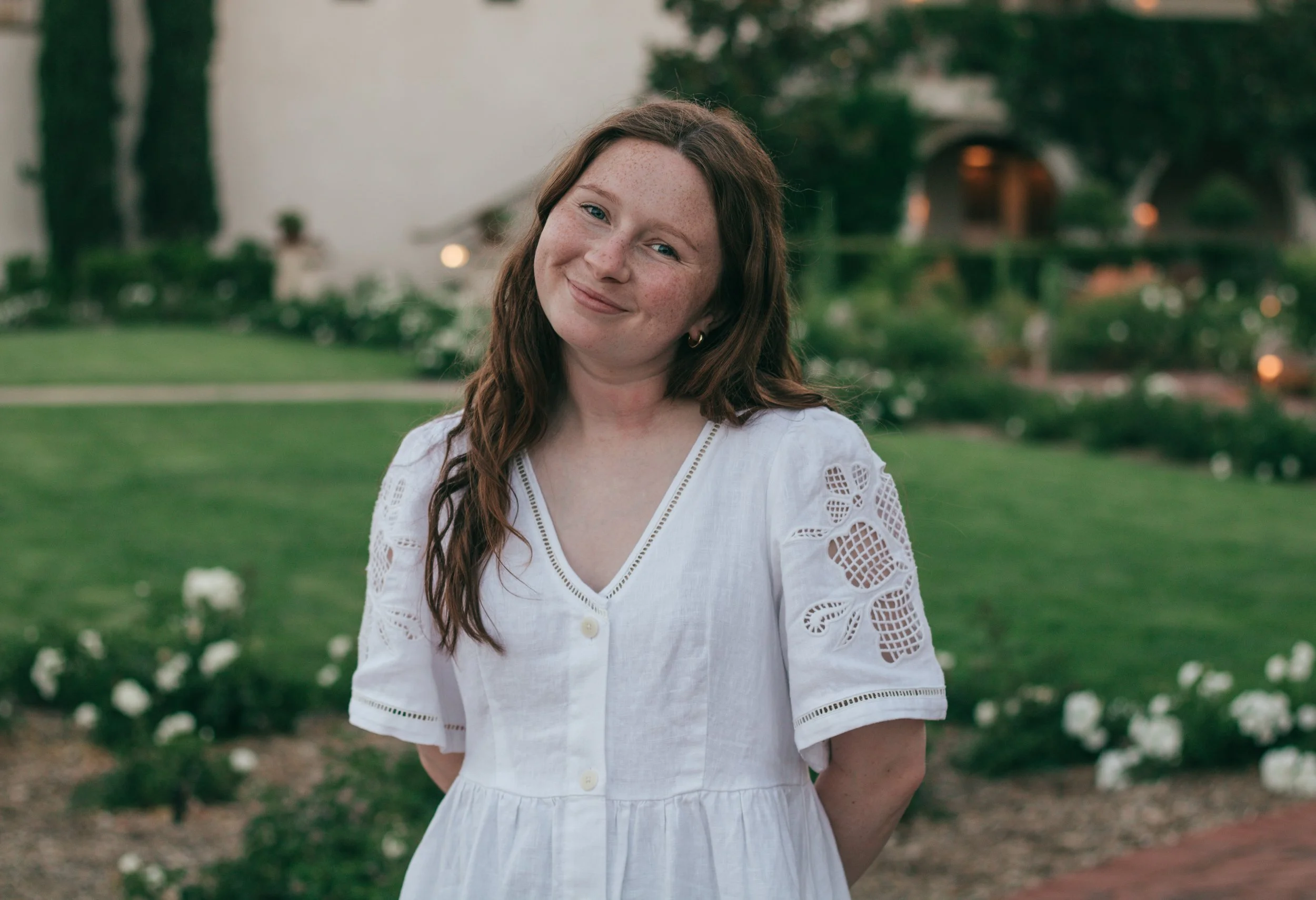Photographer smiles with a gentle head tilt in a sunlit outdoor setting, framed by warm tones and natural scenery.