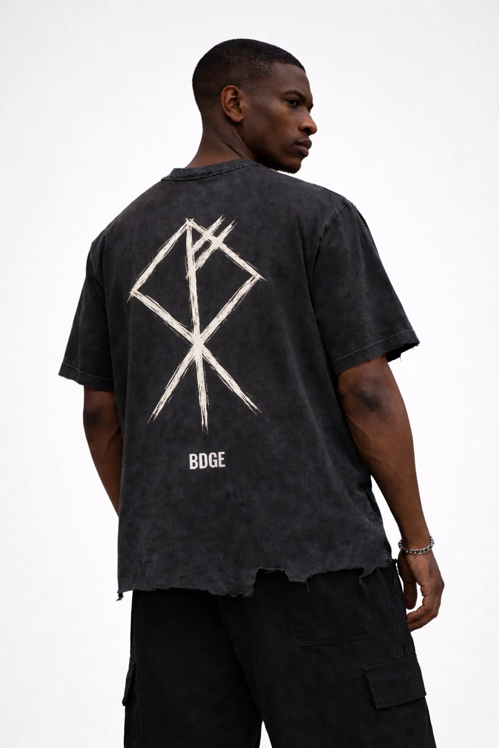 A young man in a black, distressed t-shirt with a graphic design on the back, standing against a plain white background.