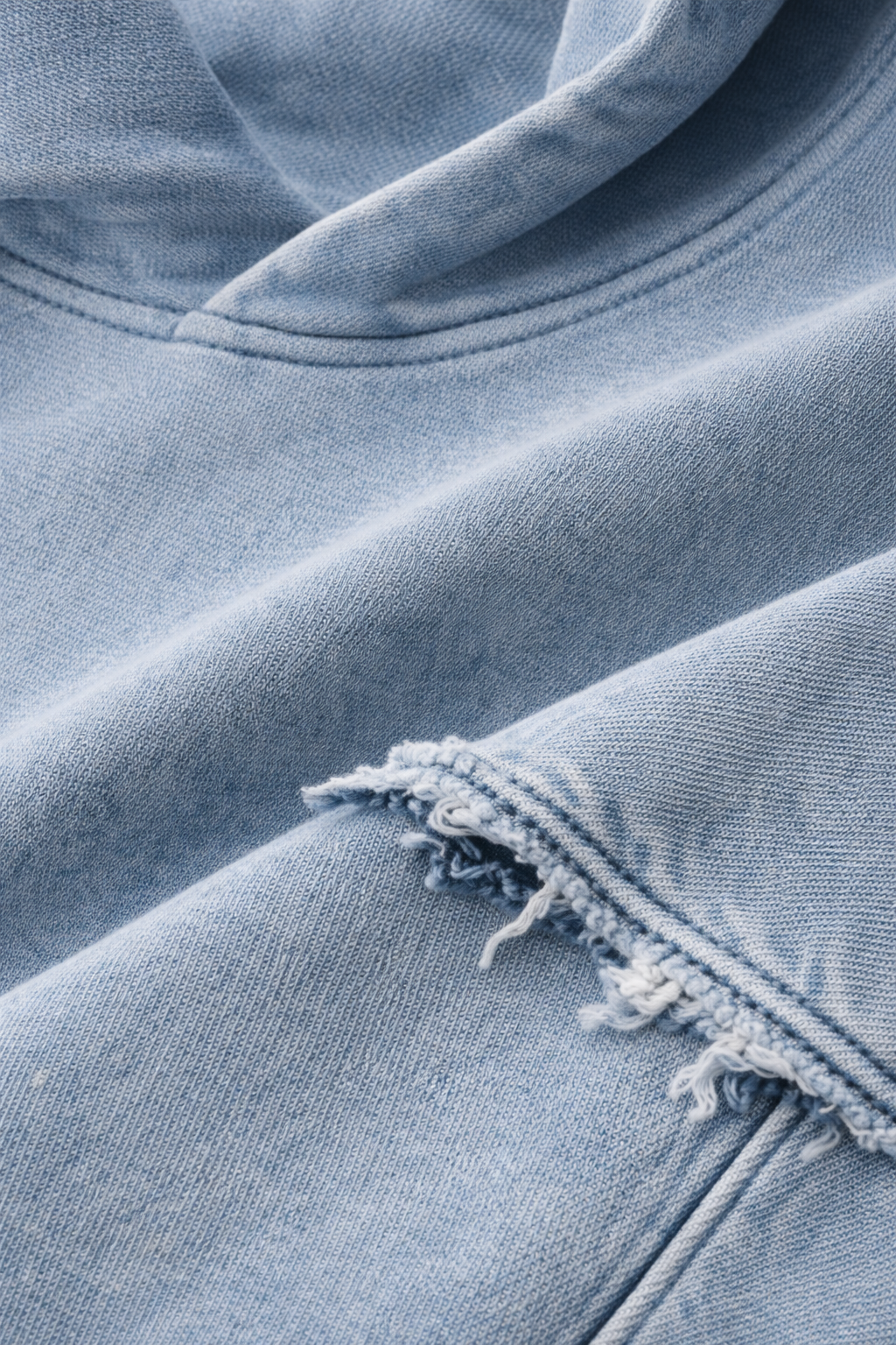 Close-up of ripped light blue denim fabric with frayed edges and visible seams.