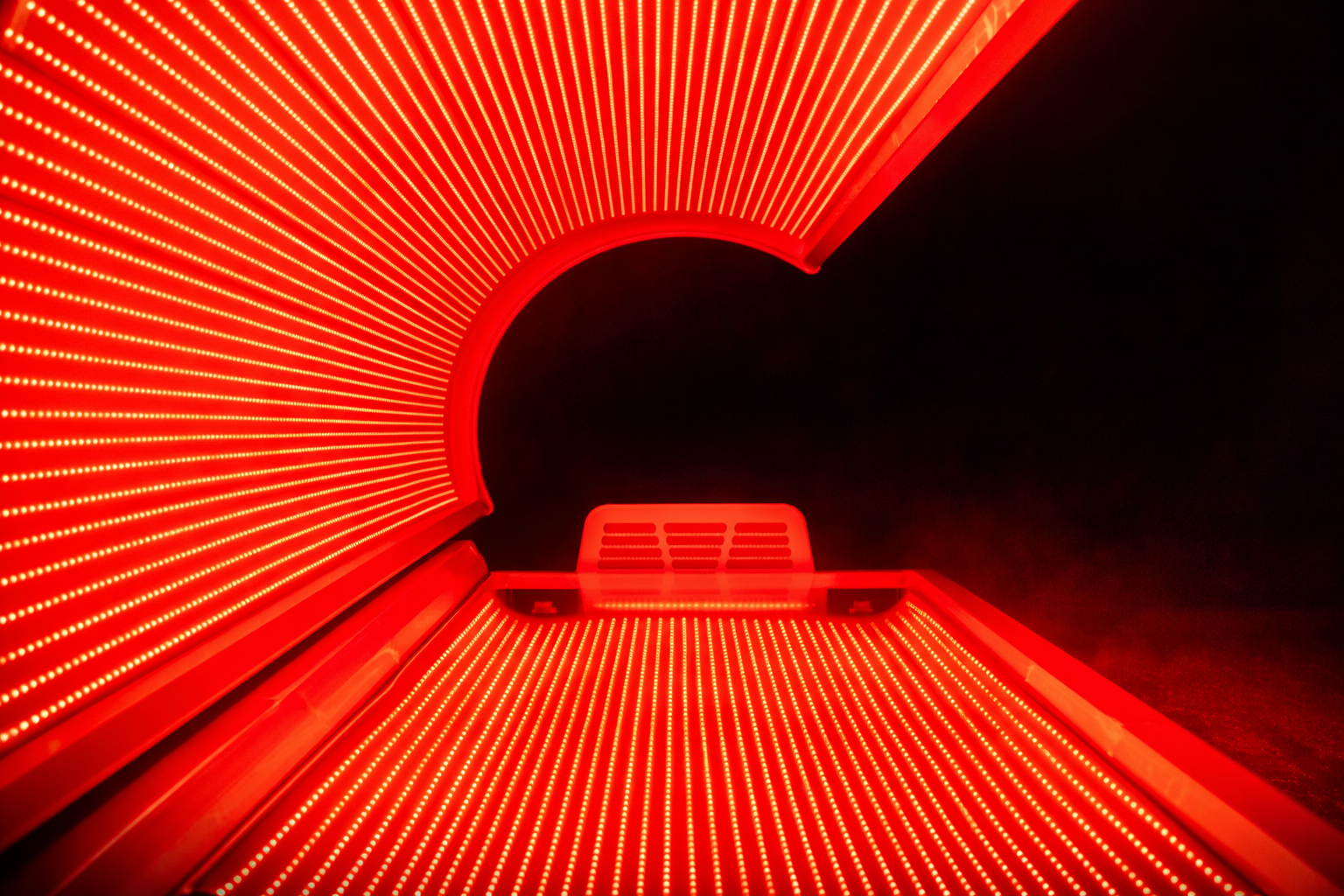 Red LED light therapy bed with glowing red lights on a black background.