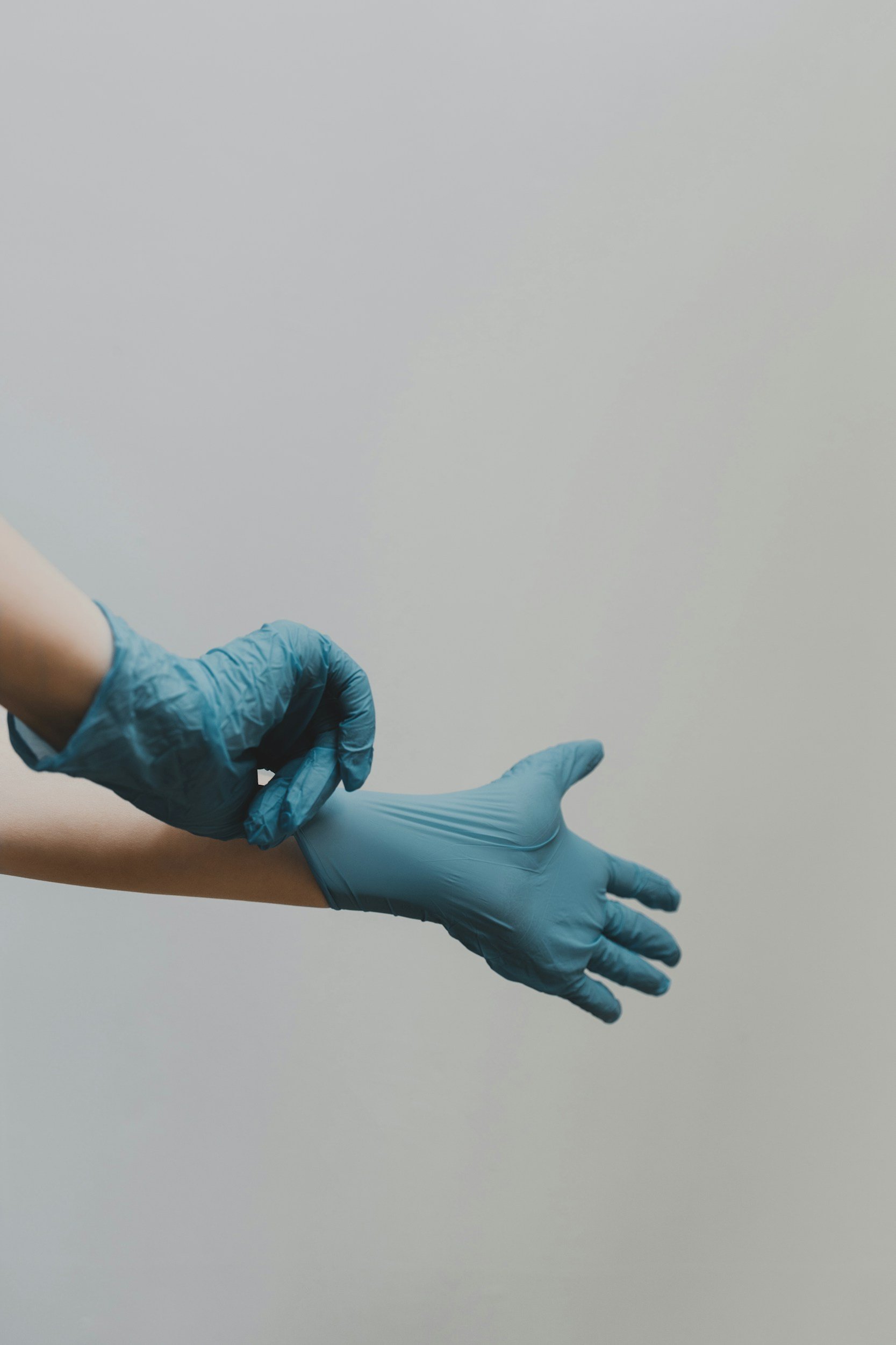 A person is putting on a blue cleaning gloves against a white background before commercial cleaning.