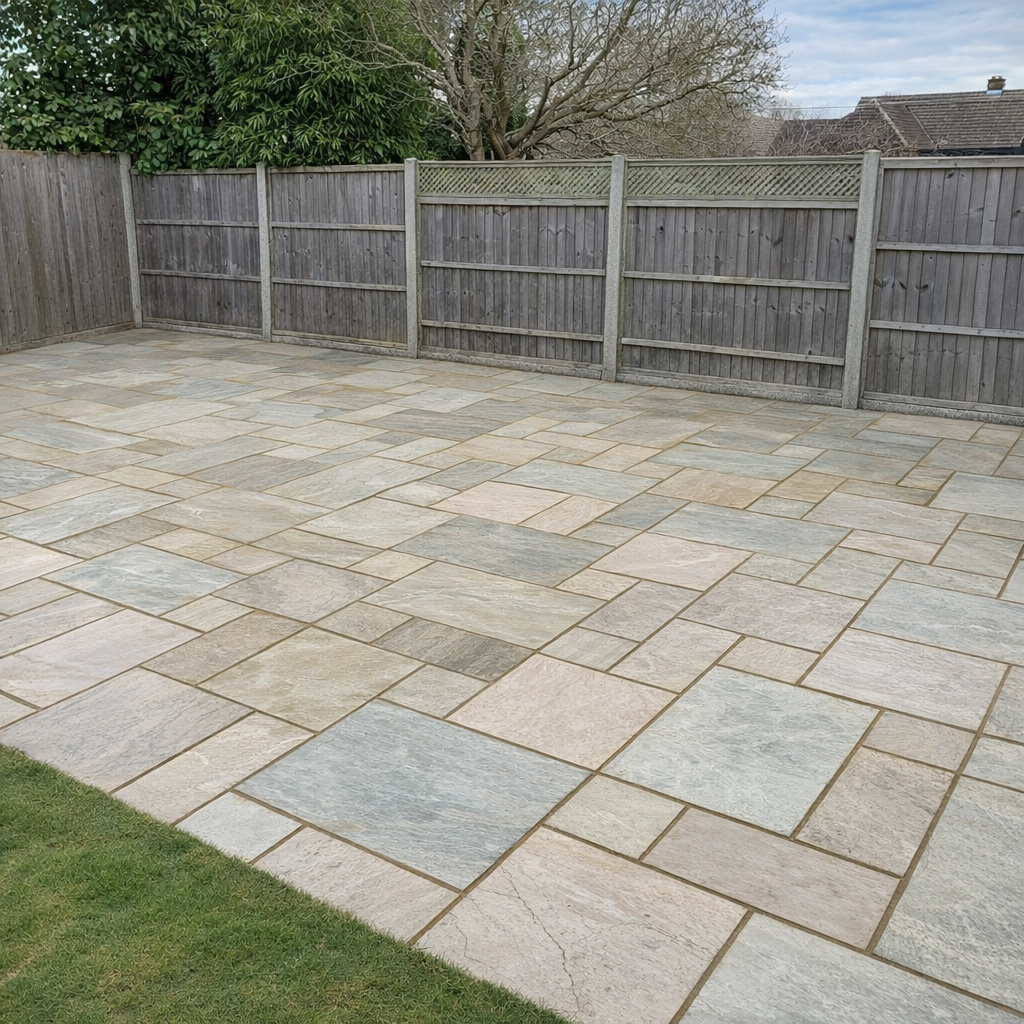 A backyard with a paved stone patio and a wooden privacy fence. There are trees and neighboring rooftops in the background.
