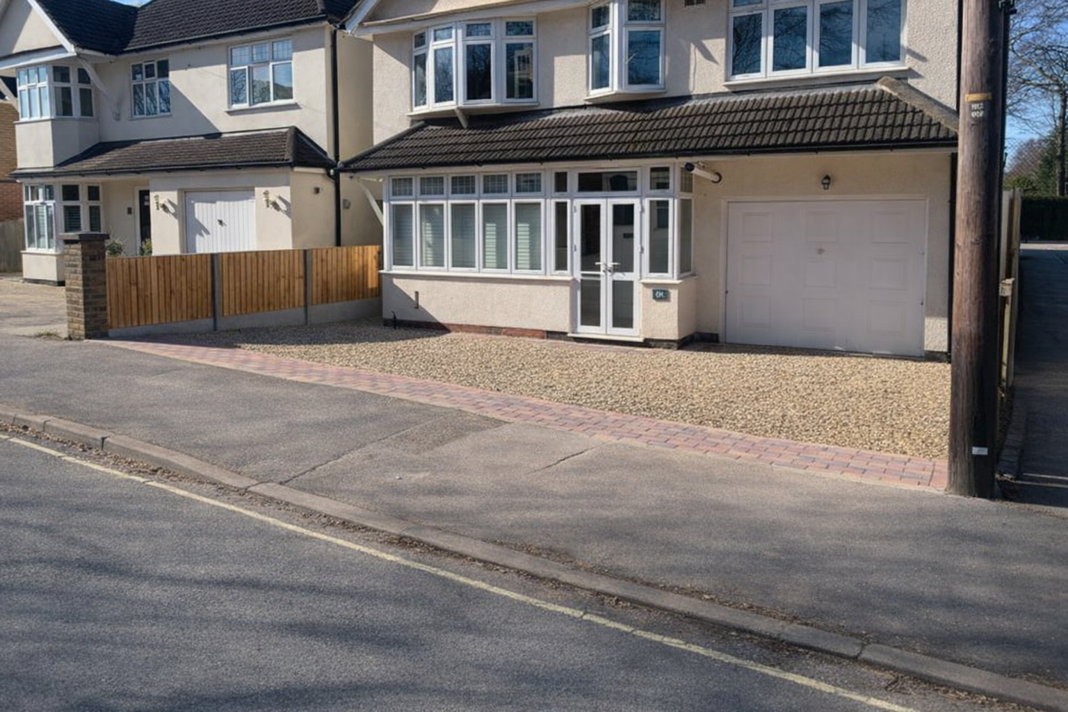 A curved area in a yard filled with small black and white pebbles, bordered by dark gray bricks, with green bushes and plants along a wooden fence in the background.