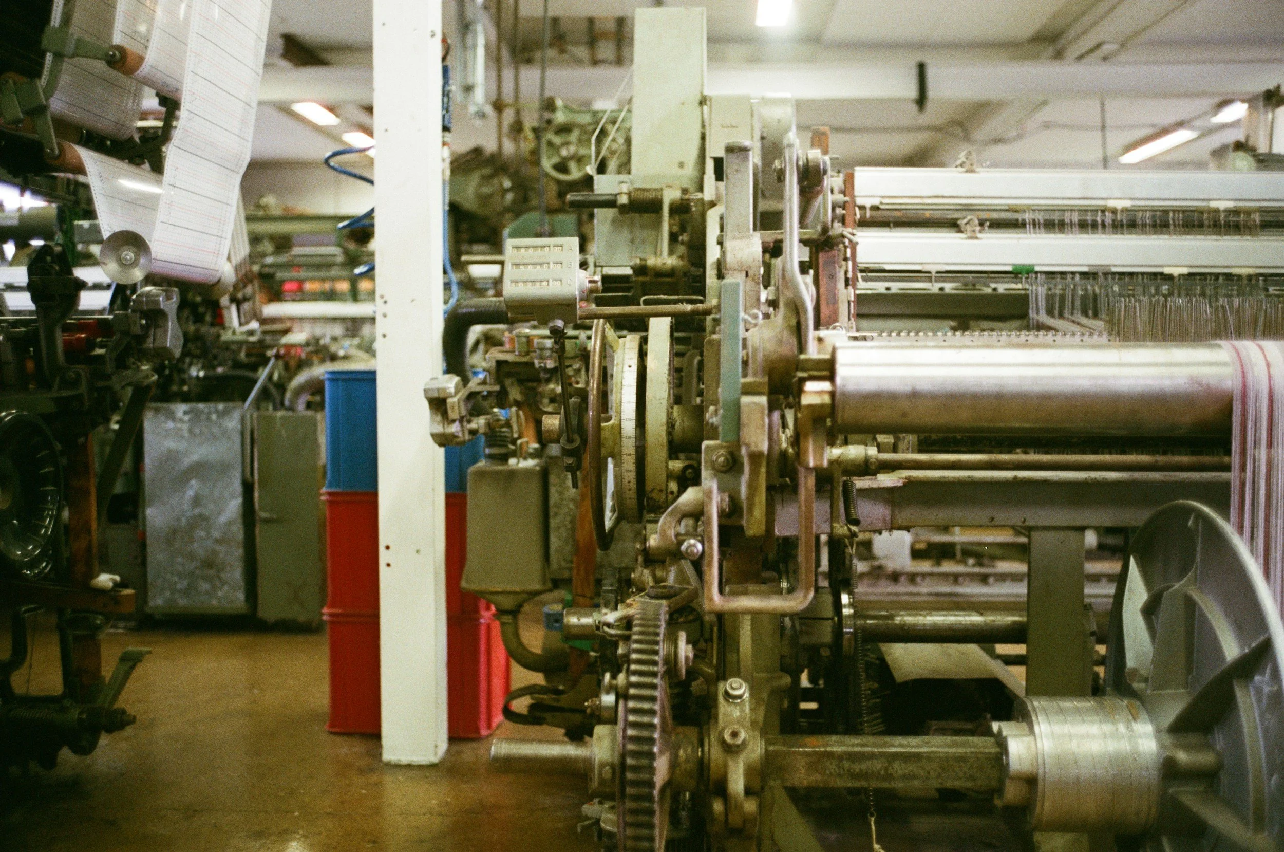 Industrial textile machine with spools of thread and machinery components in a factory setting.