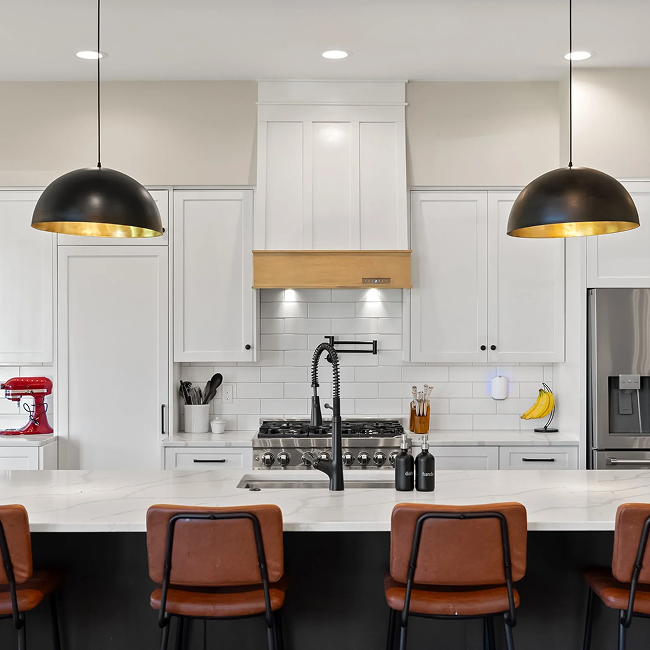Modern kitchen with white cabinets, a white countertop, black pendant lights, and a stainless steel refrigerator. There is a black faucet, a red stand mixer, and bananas on the counter.
