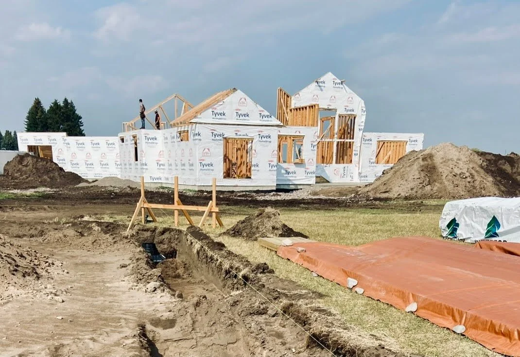 Back elevation of a house under construction with wooden framing and multiple rooms in progress.