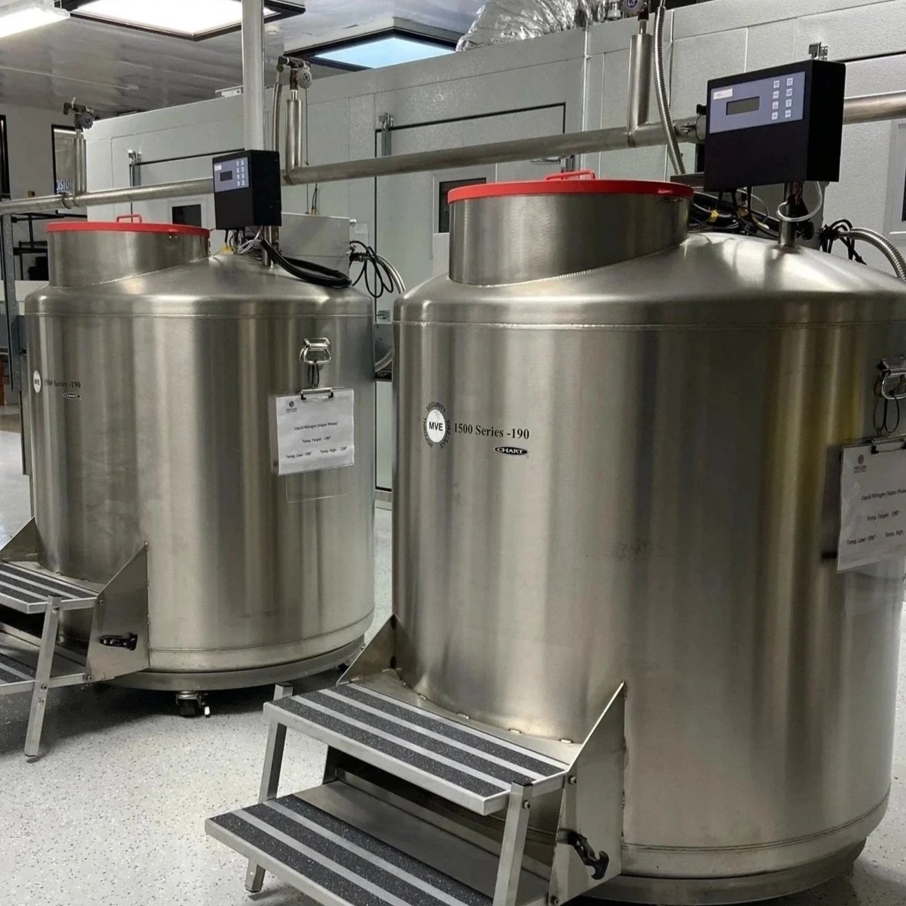 Two large stainless steel cryogenic tanks, labeled '1500 Series - 190,' connected by pipes and digital control panels, situated in a clean, biorepository.