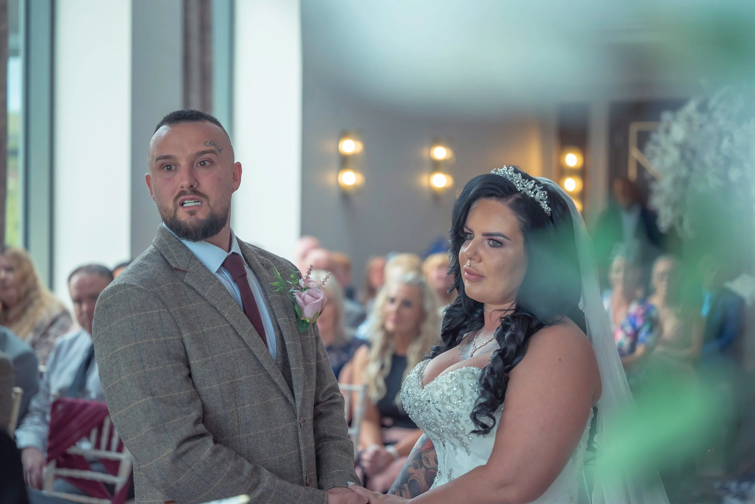 Bride and groom holding hands during their wedding ceremony in a modern venue with guests watching.