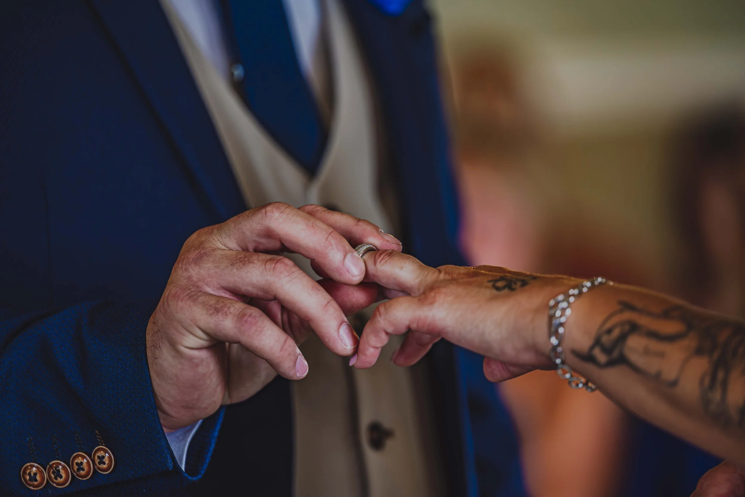 Close-up of a wedding couple exchanging rings, with the groom placing a ring on the bride's finger.