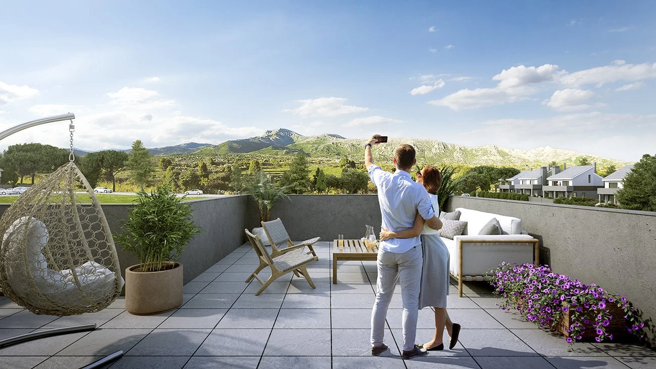 Pareja en la terraza tomando una selfie con fondo de montañas y cielo soleado.