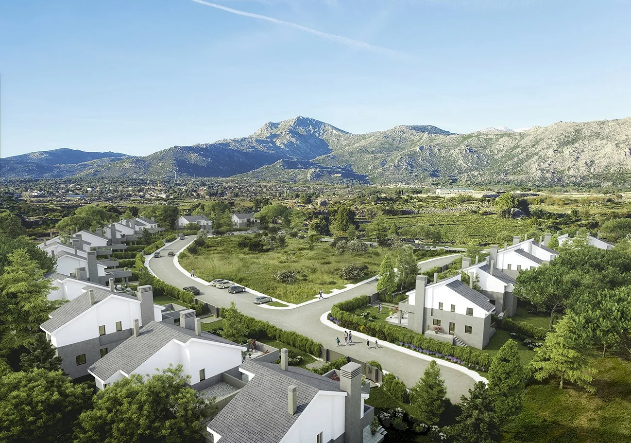 Conjunto de casas blancas con techos grises en un área rural, rodeadas de árboles y una carretera que las conecta, con montañas en el fondo bajo un cielo despejado.