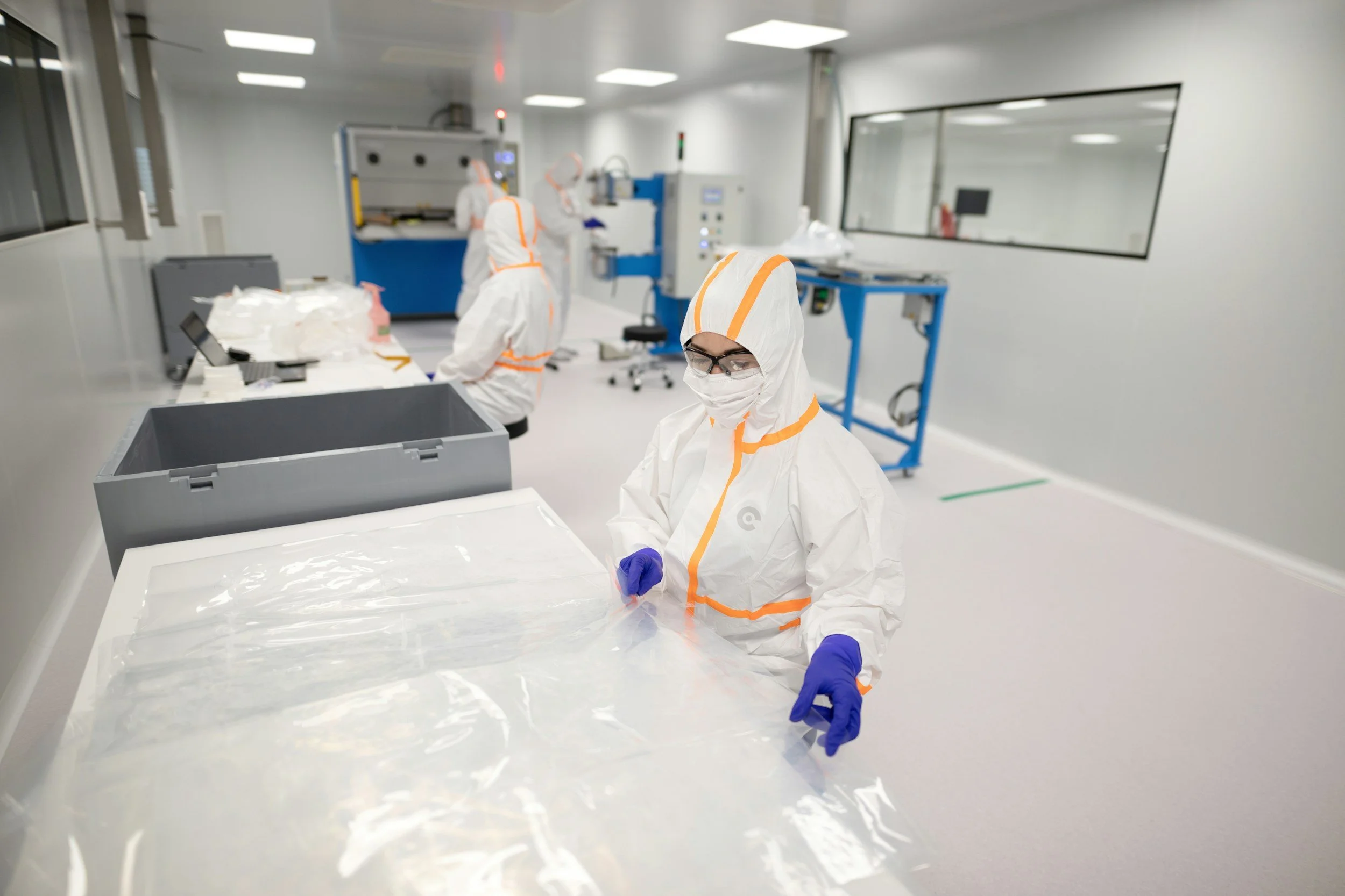 Scientists in cleanroom suits working with materials and equipment in a laboratory or manufacturing facility.