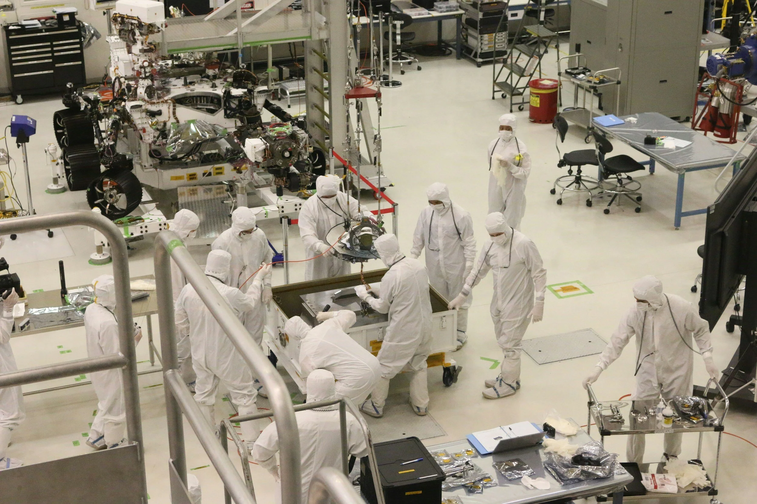 Scientists and engineers in white protective suits working in a clean room at a NASA space facility, assembling or maintaining spacecraft components.