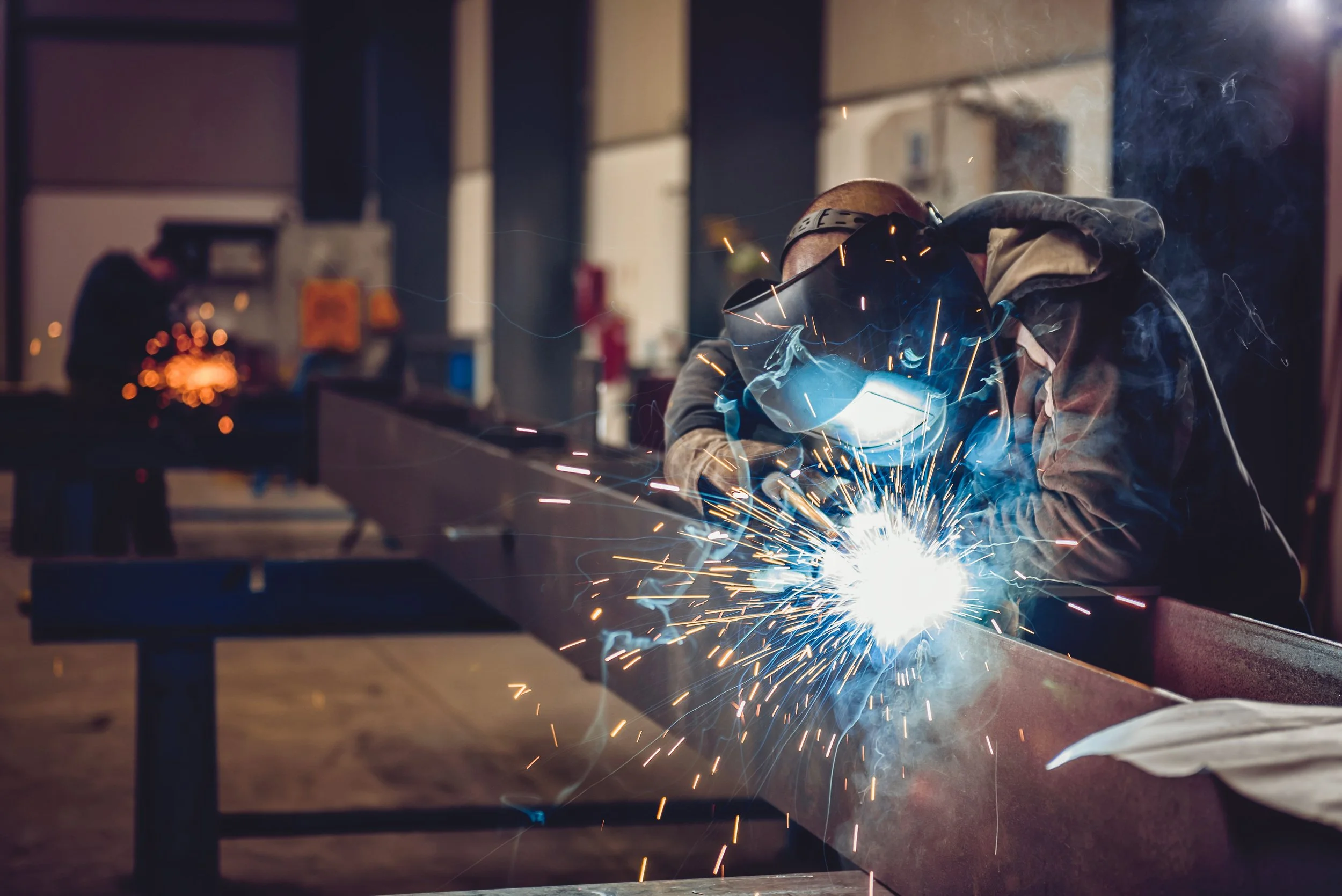 A person welding metal in a workshop, wearing protective gear and creating sparks.