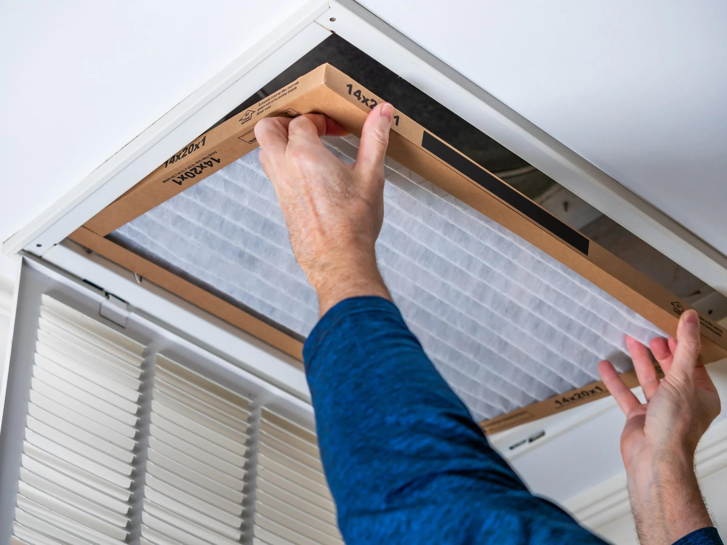 Person installing an air filter into an air conditioning vent in a ceiling.
