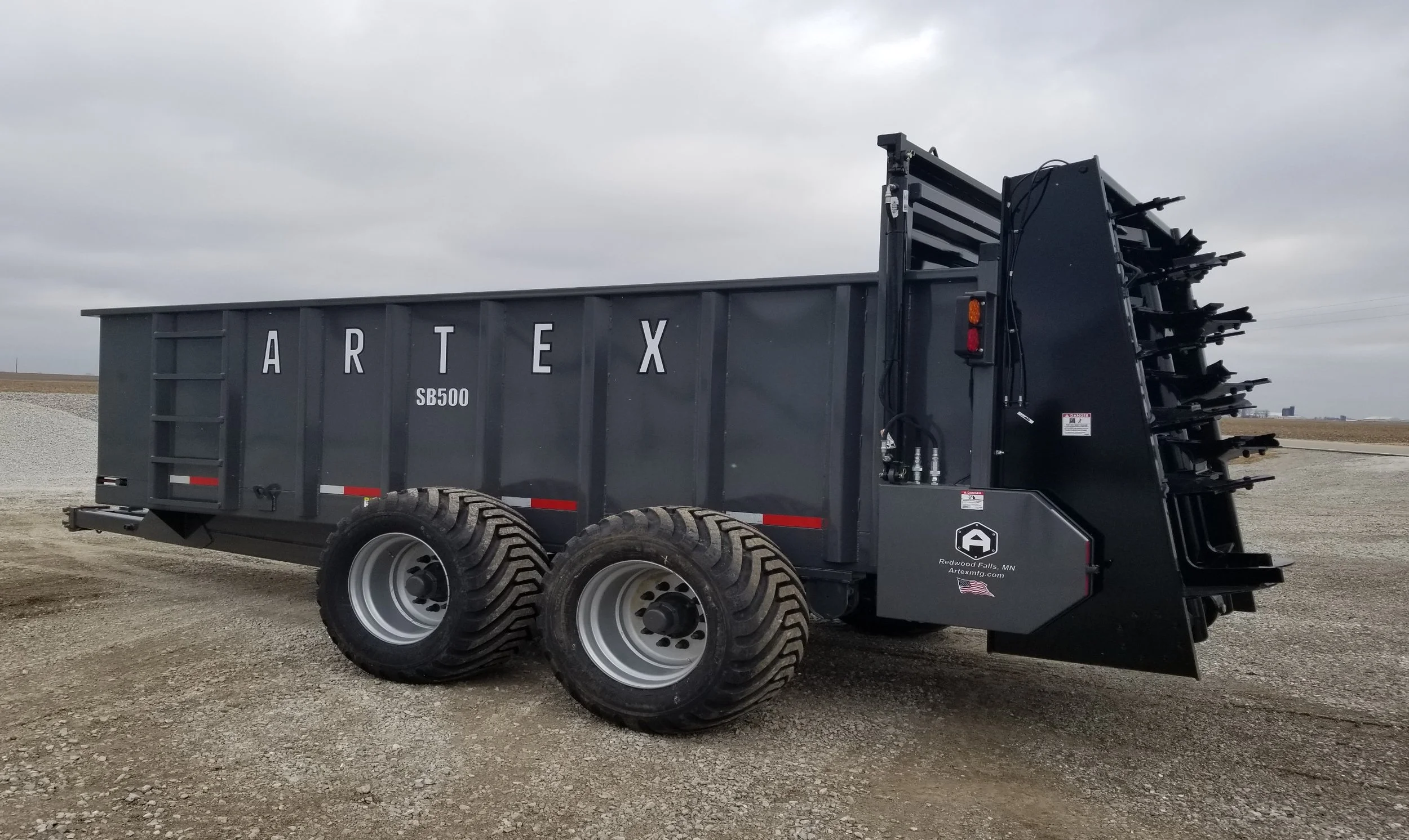ARTEX manure spreader model number 'SB500', parked on a gravel surface under a cloudy sky in Reedsburg Falls, Minnesota.