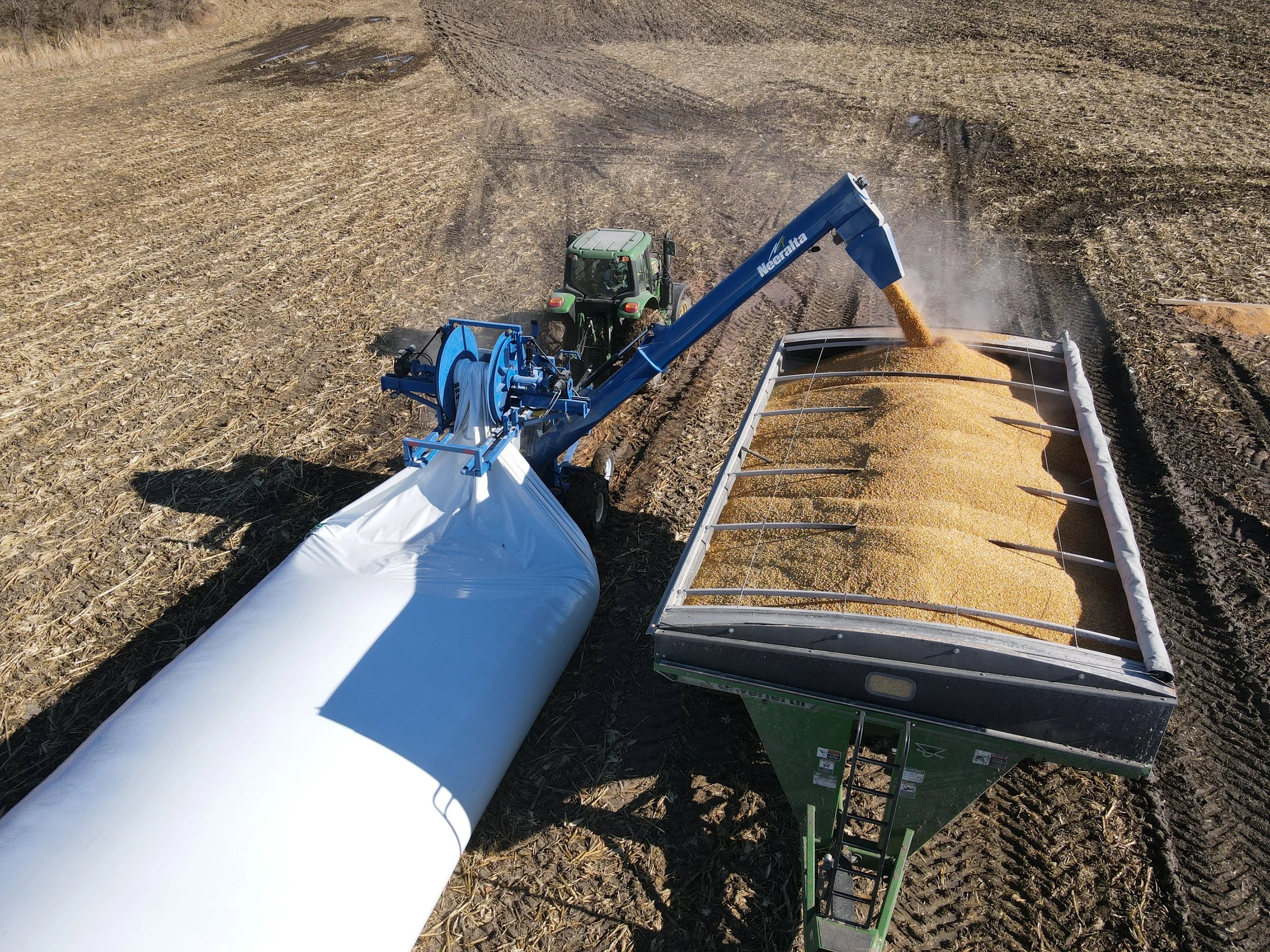 Neeralta on a green John Deere tractor in an industrial lot with buildings, trucks, and cars in the background.