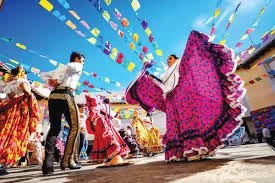 People dancing in traditional Mexican clothing at a colorful outdoor festival.