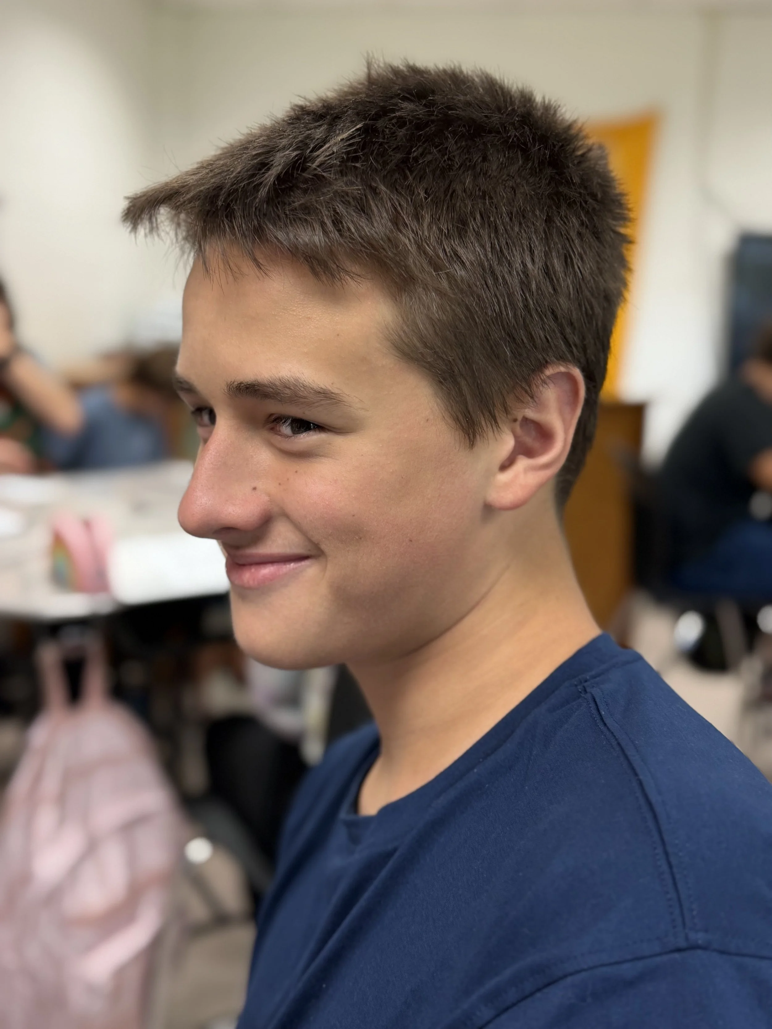 Side profile of a young man with short brown hair in a classroom setting.