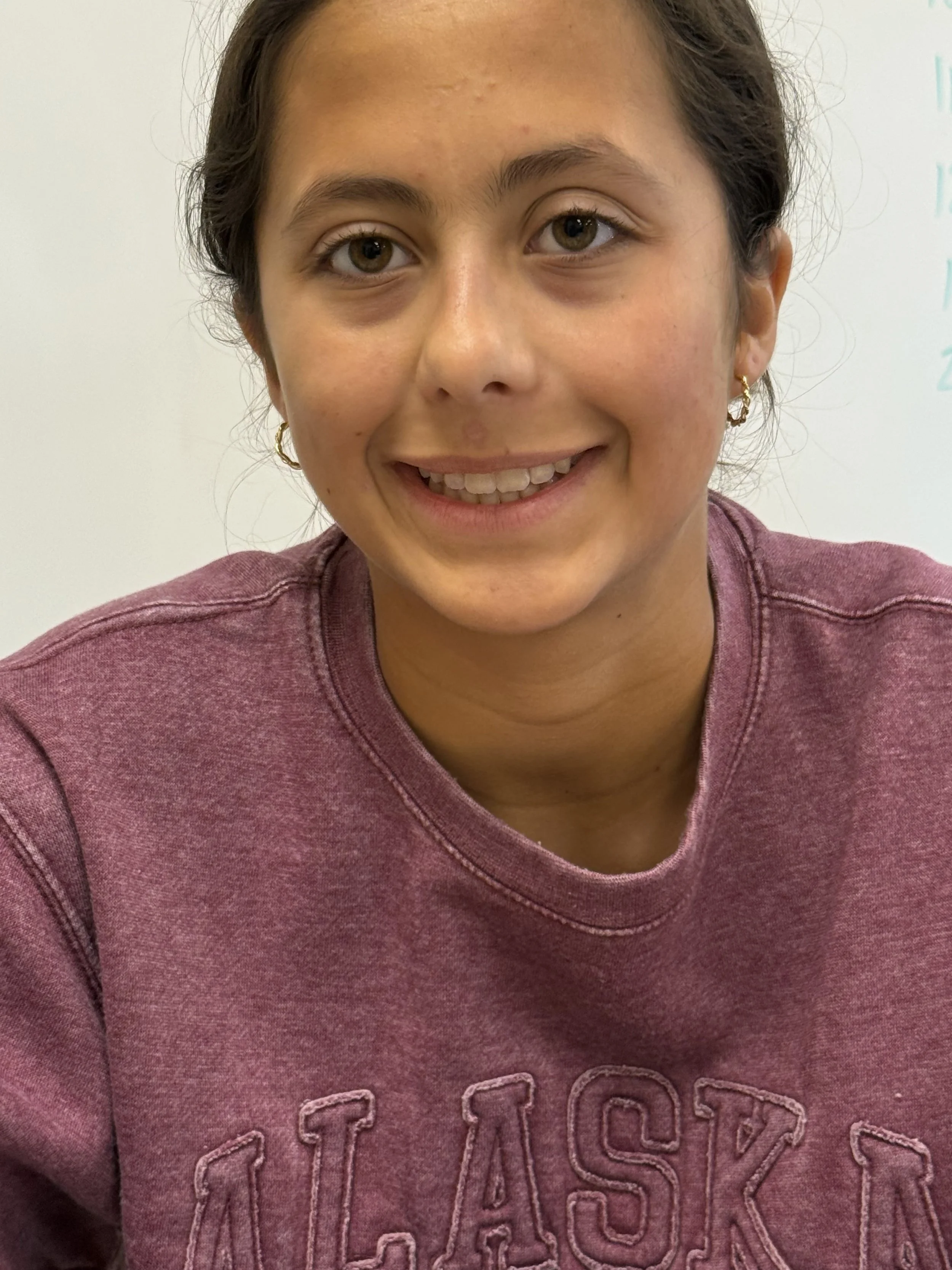 Smiling girl with braces and long brown hair in a classroom.