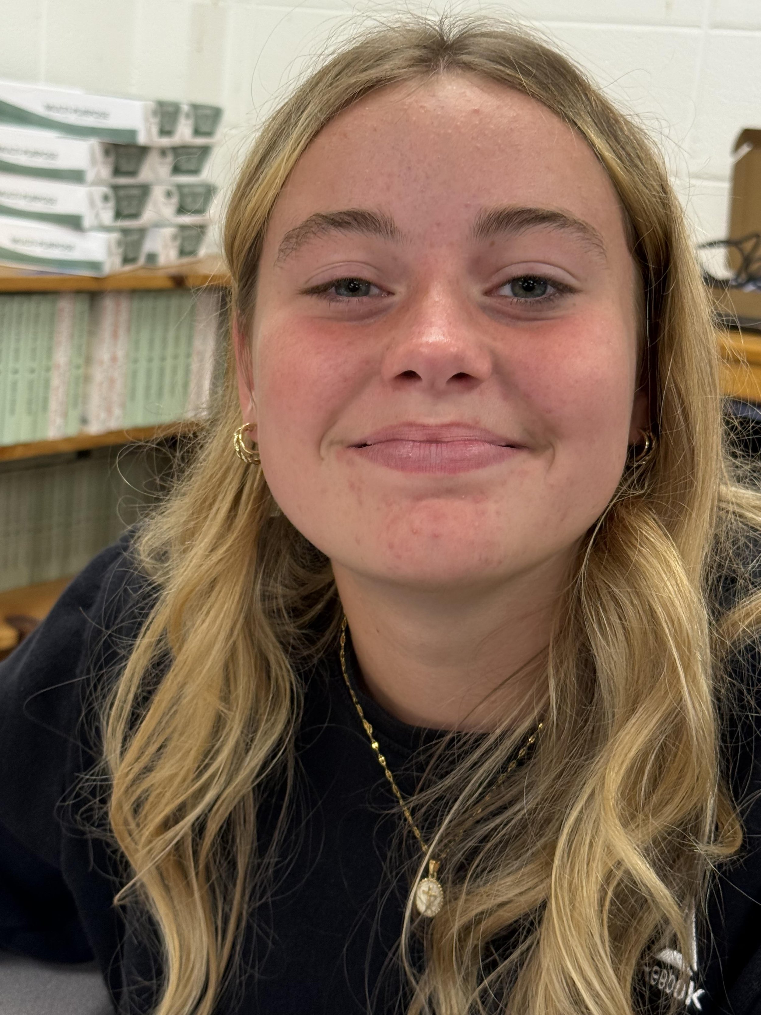 Close-up of a young woman with blonde hair, blue eyes, and a slight smile, wearing a pink shirt.
