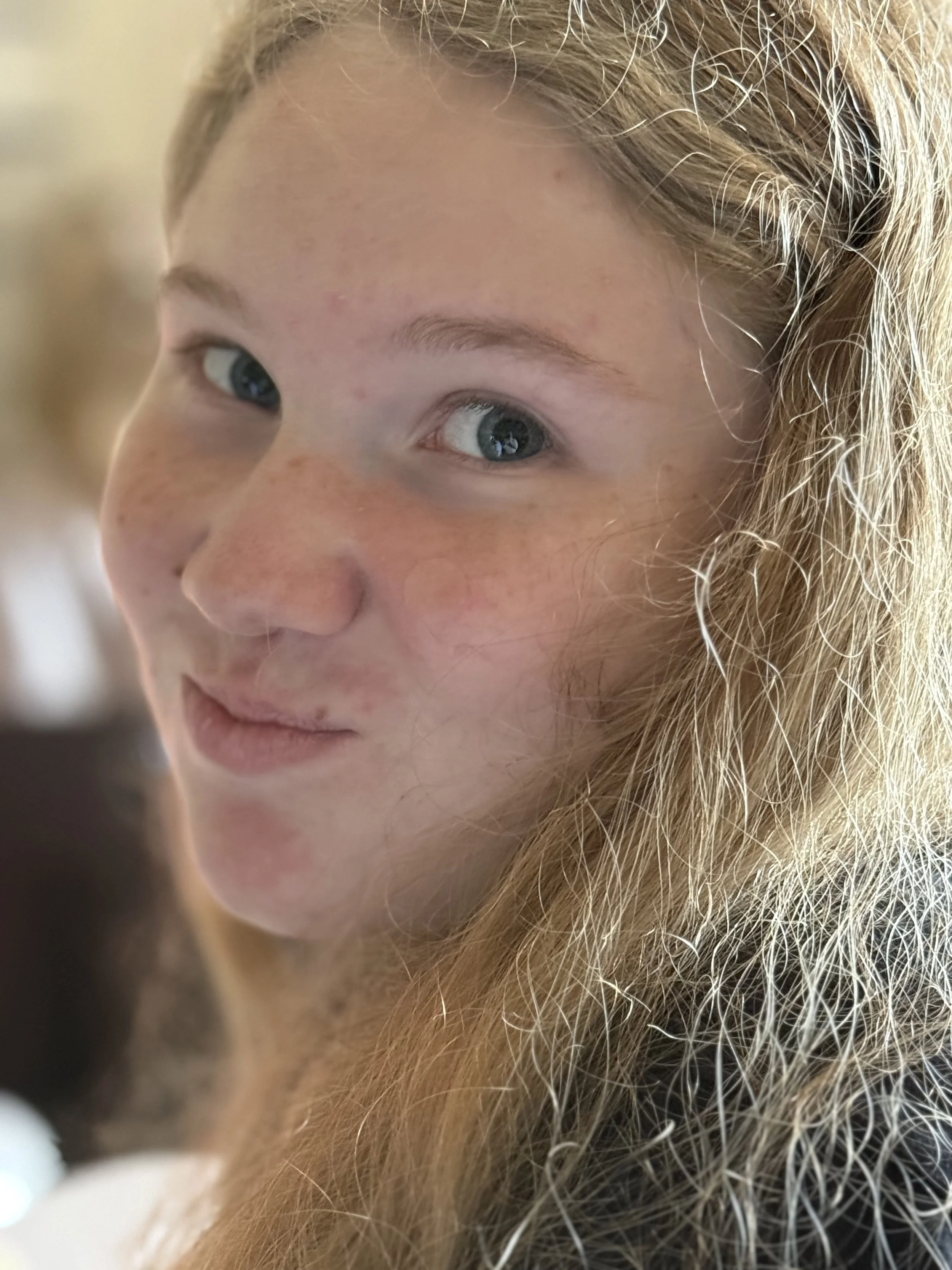Close-up of a young woman with light skin, blue eyes, and long, wavy blonde hair smiling softly.
