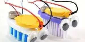 Two homemade robots made from plastic bottle caps, wires, and yellow batteries, resembling small cartoonish creatures.