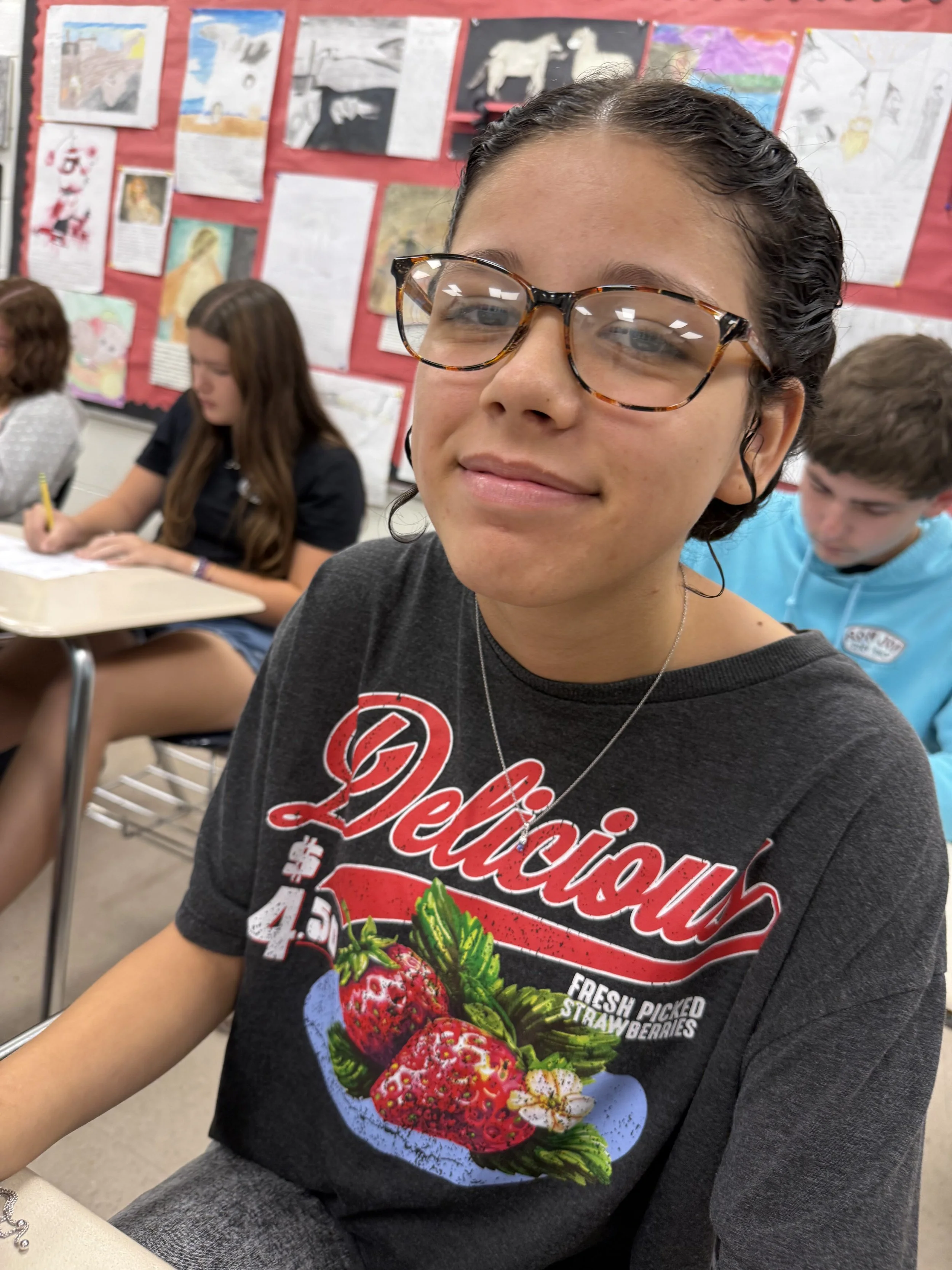 Close-up of a young person's face wearing clear glasses, with brown hair slicked back and a slight smile.