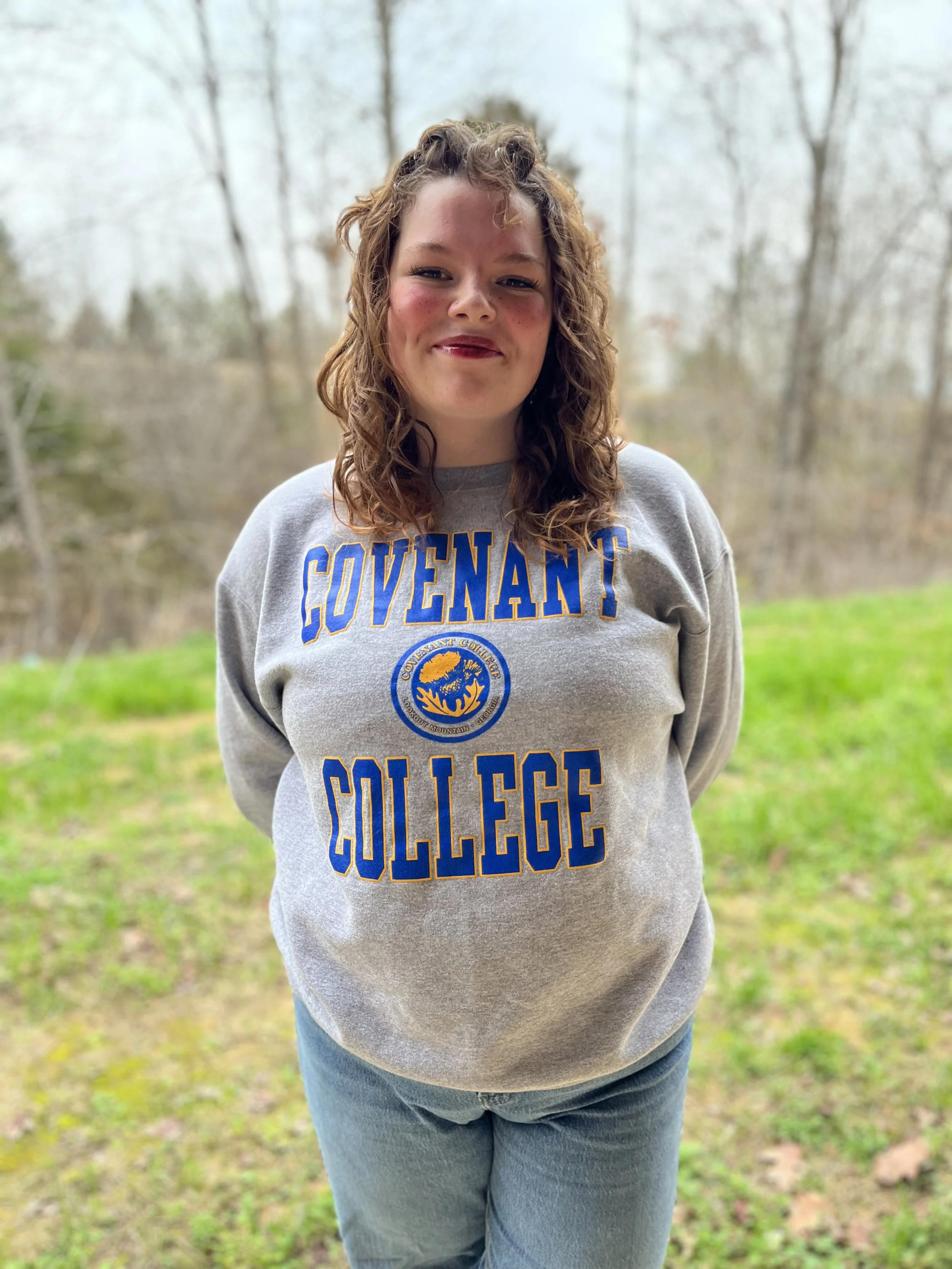 Smiling woman with curly hair wearing a college hoodie in a classroom.