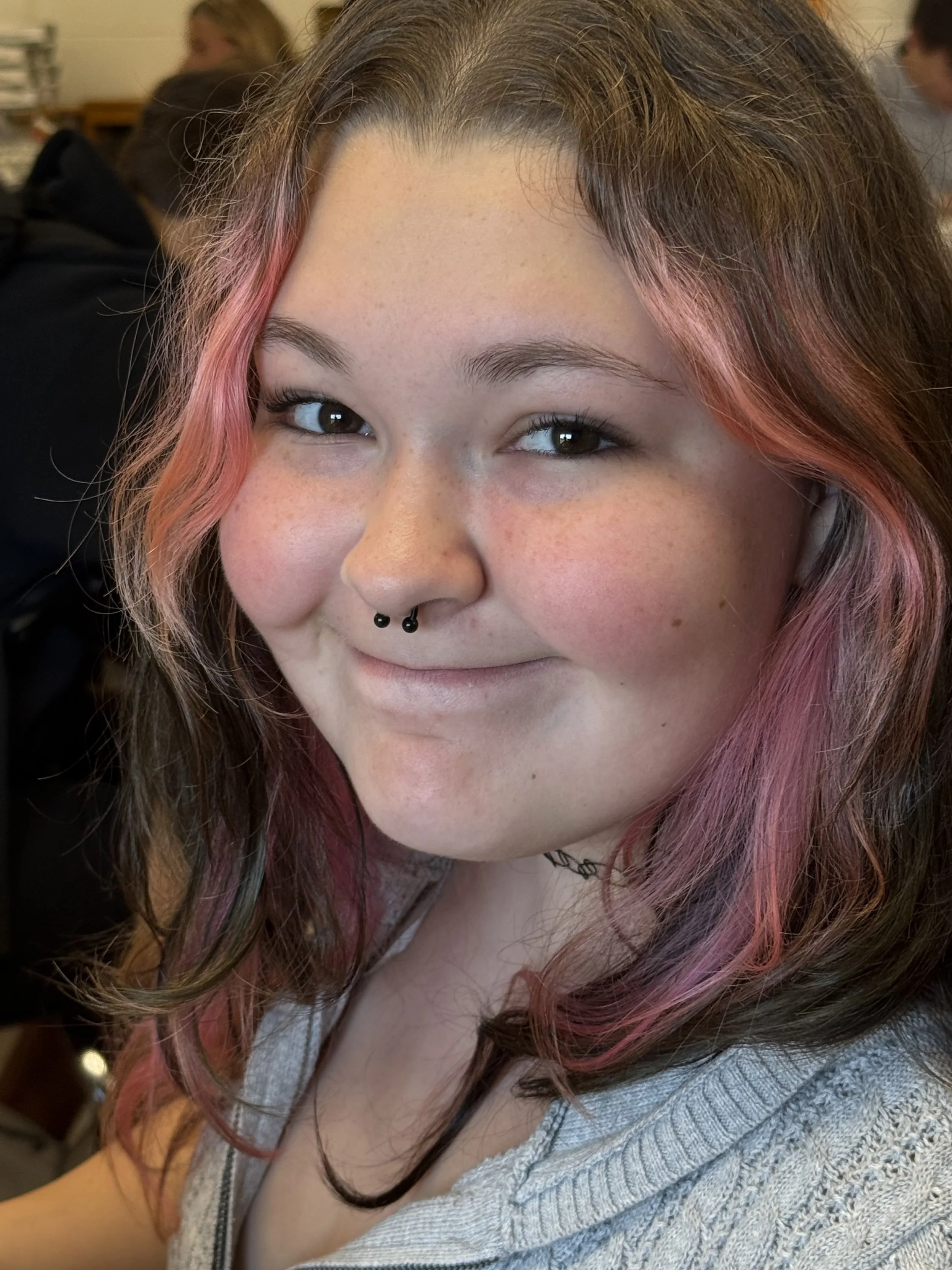 A young woman with black hair dyed blue at the tips, wearing a purple sweatshirt with a graphic design and the words 'Olivia' on it. She is making a sad or disappointed facial expression.