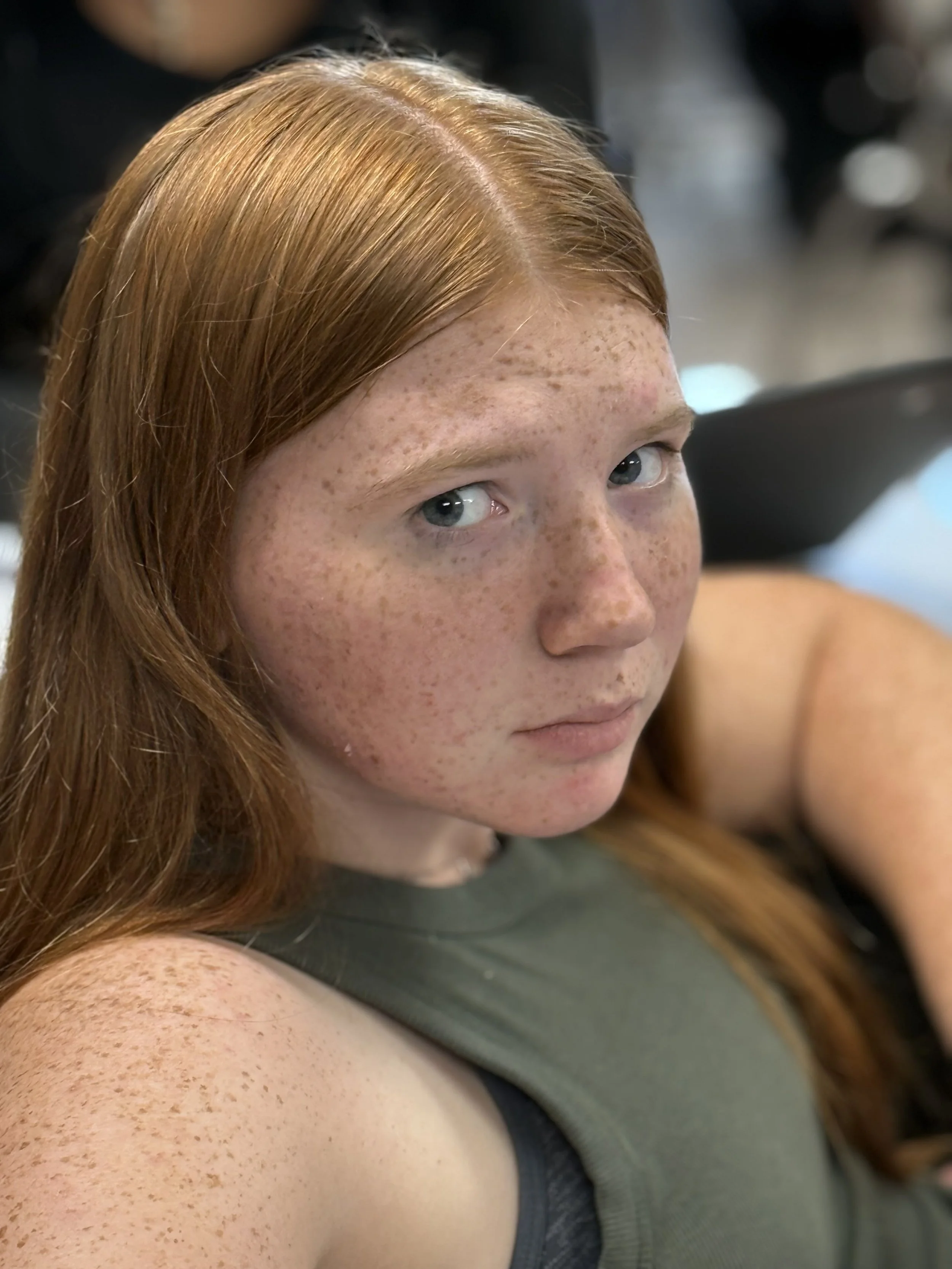 A young woman with red hair and freckles looking at the camera.