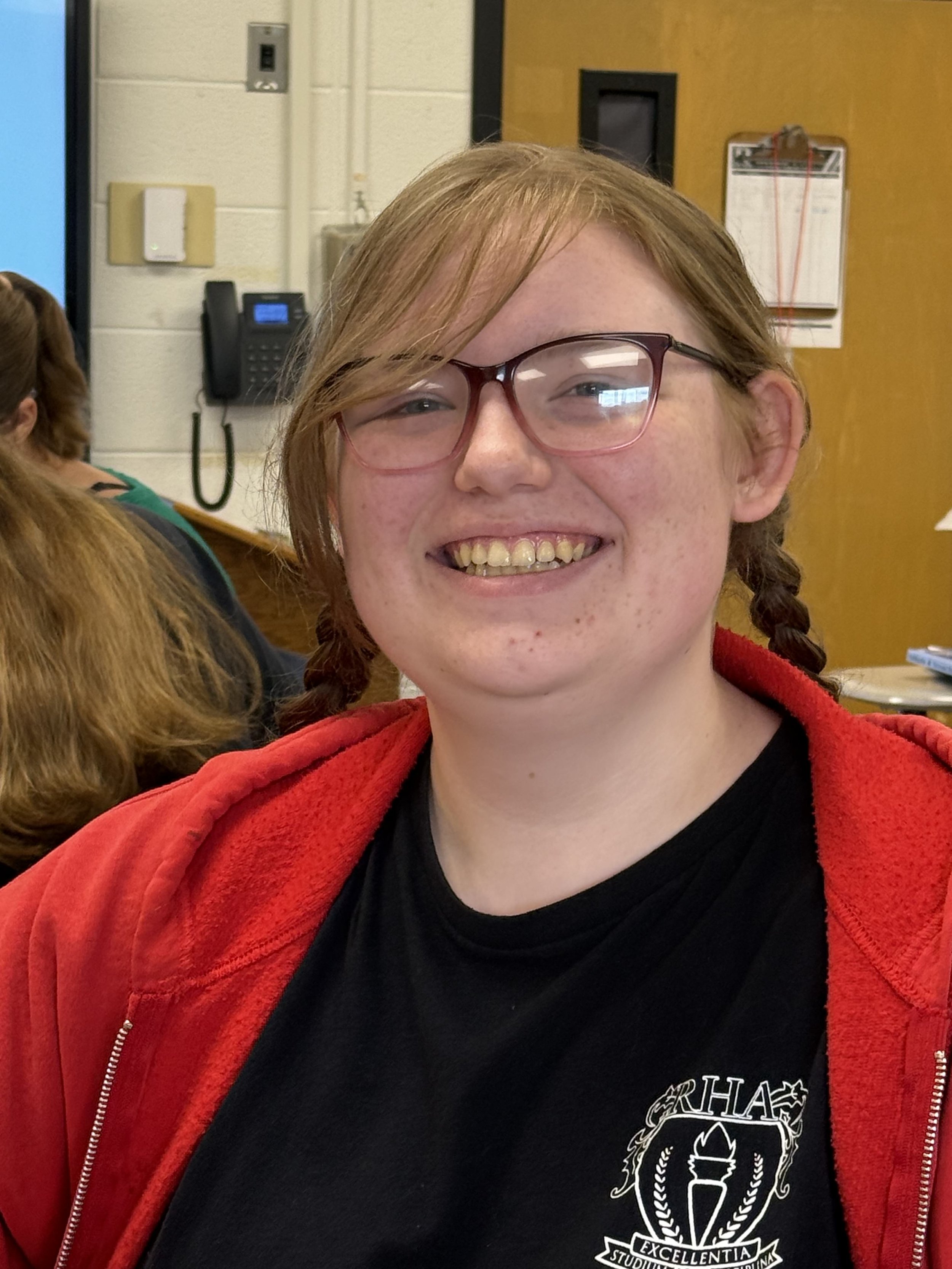 Close-up of a smiling woman with glasses and red hair, showing her teeth, with face freckles and short hair, indoors.