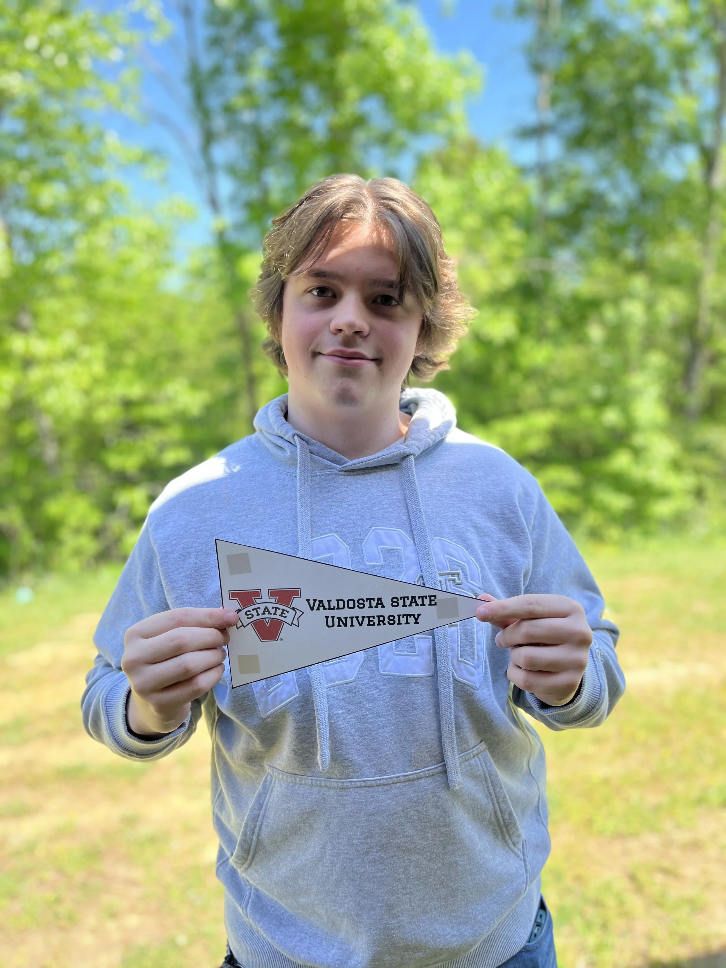 Young man with long brown hair, wearing a Georgia Bulldogs cap with 'National Champions' embroidered on it and a Nike logo, smiling at the camera in an indoor setting.
