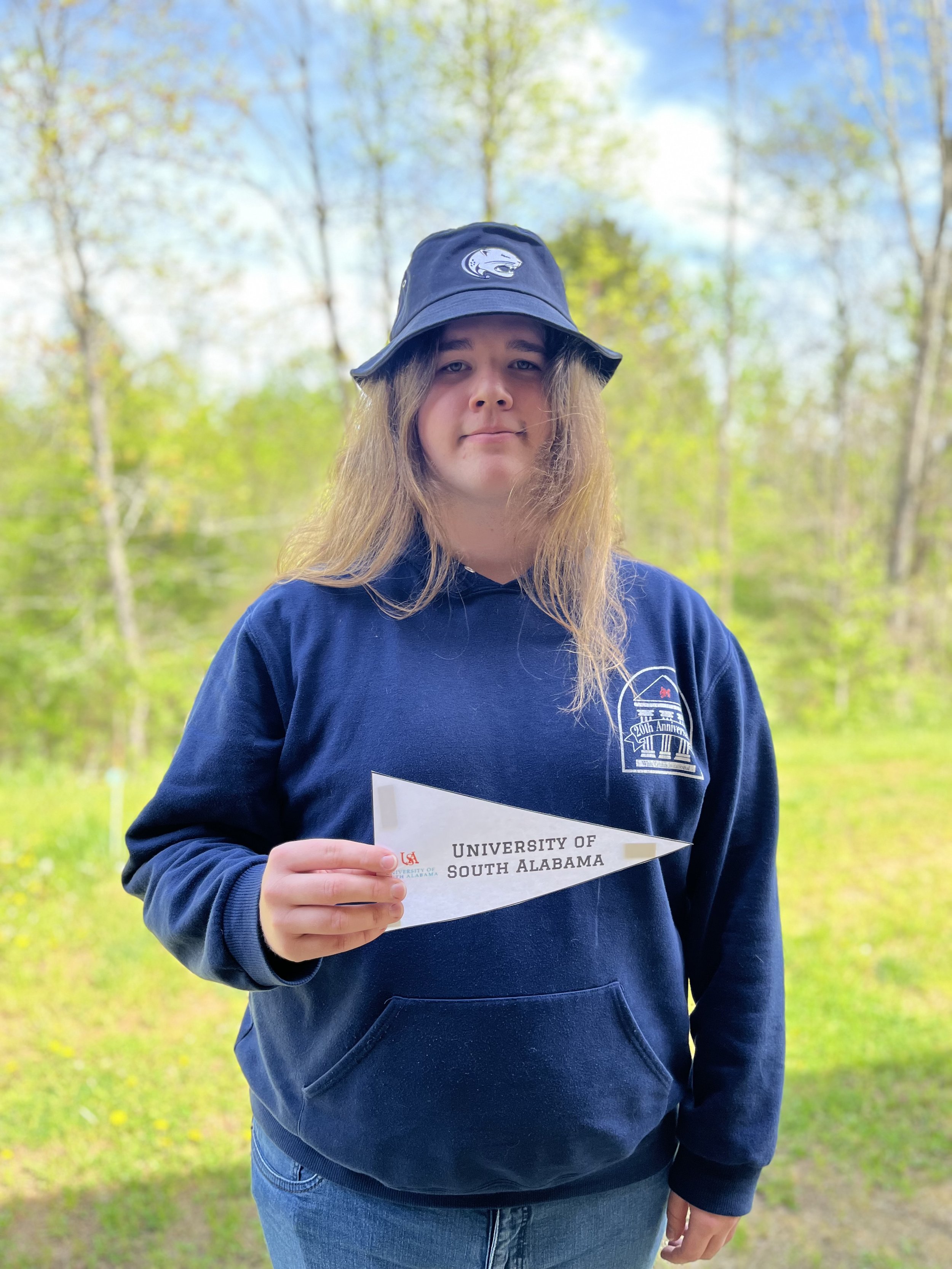 A young man with long hair and a slight beard wearing a plaid shirt, looking slightly to the side with a subtle smile.