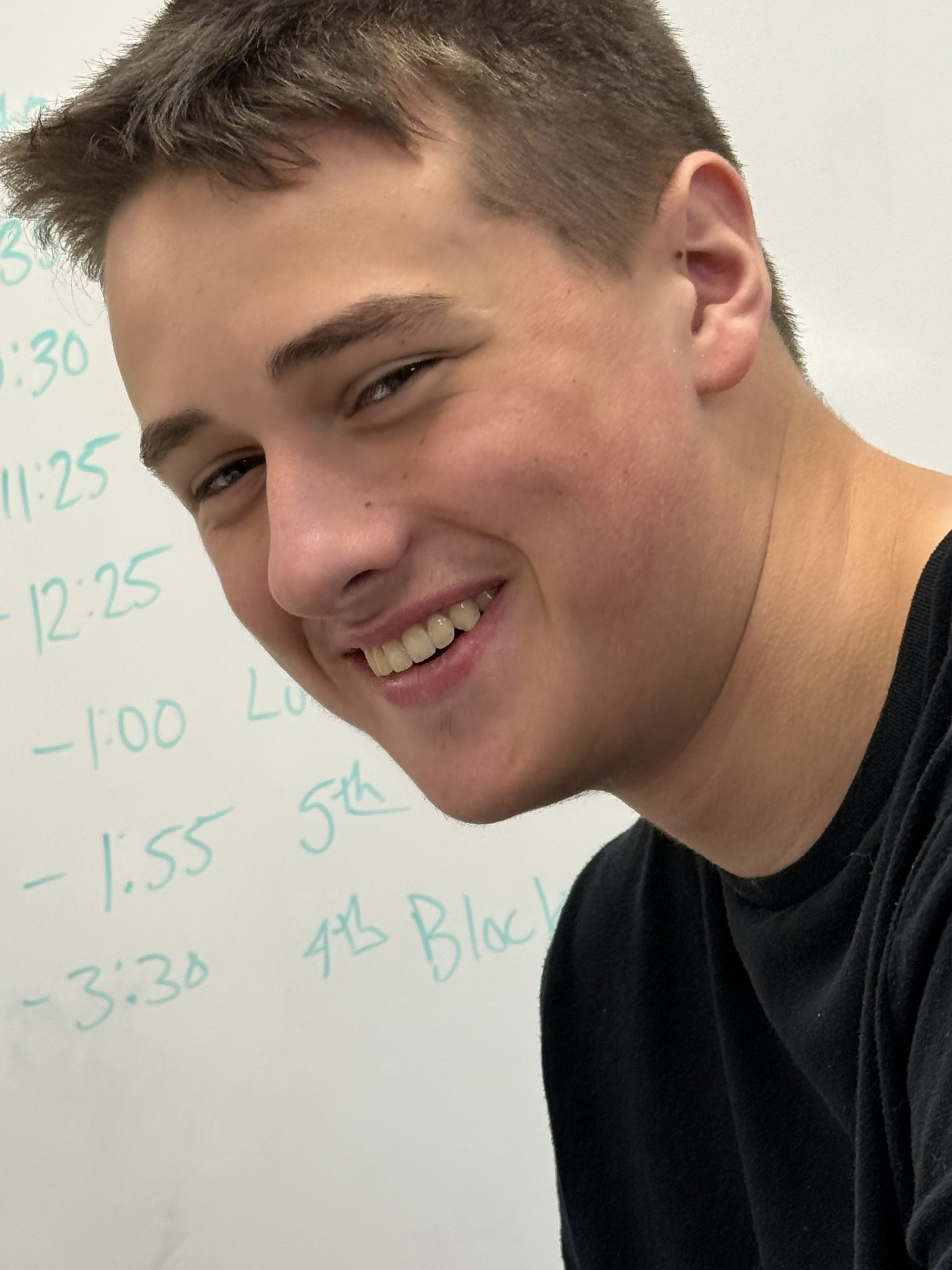 Side profile of a young man with short brown hair in a classroom setting.